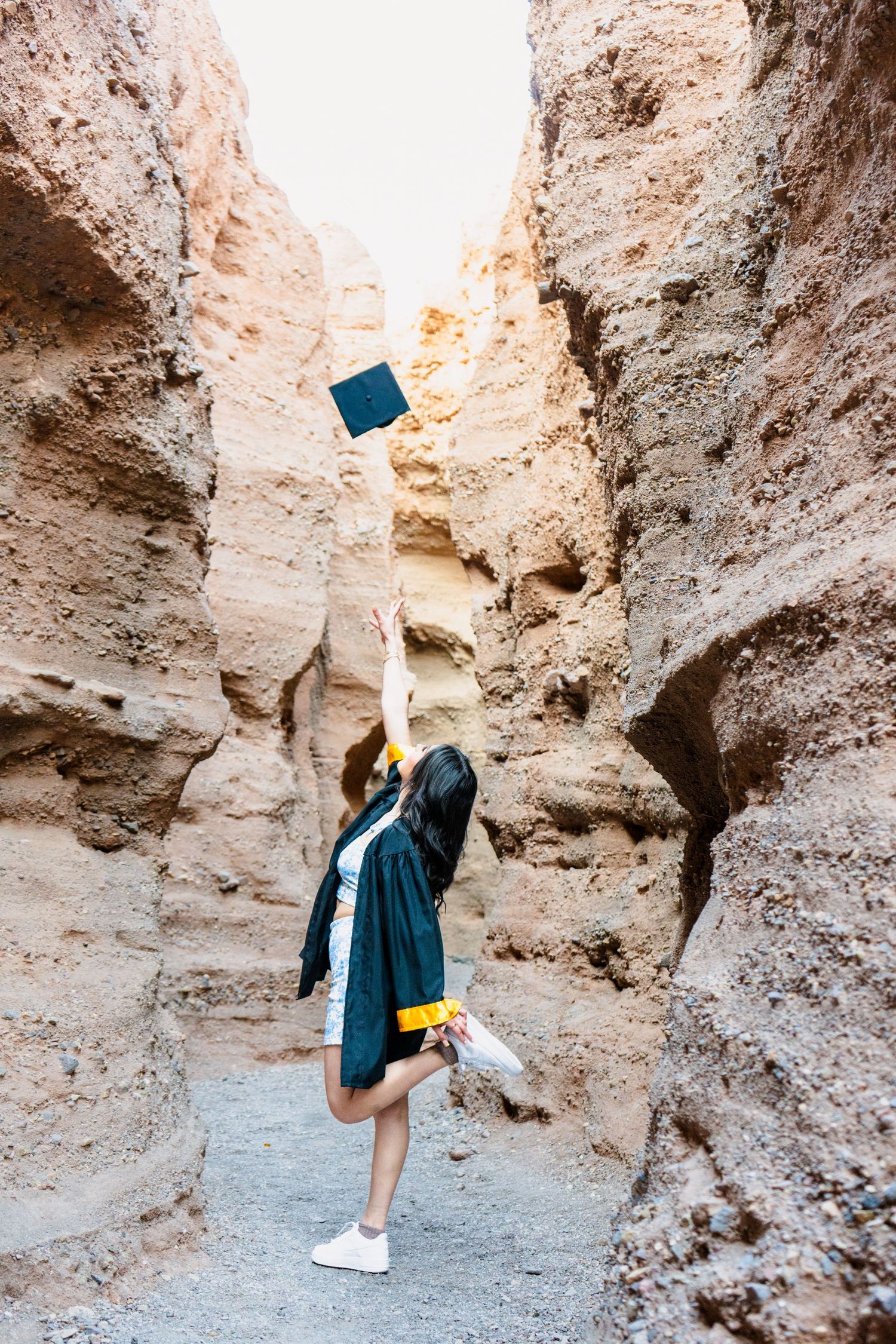 Female graduate tossing mortarboard cap into the air inside a dramatic sandstone canyon.