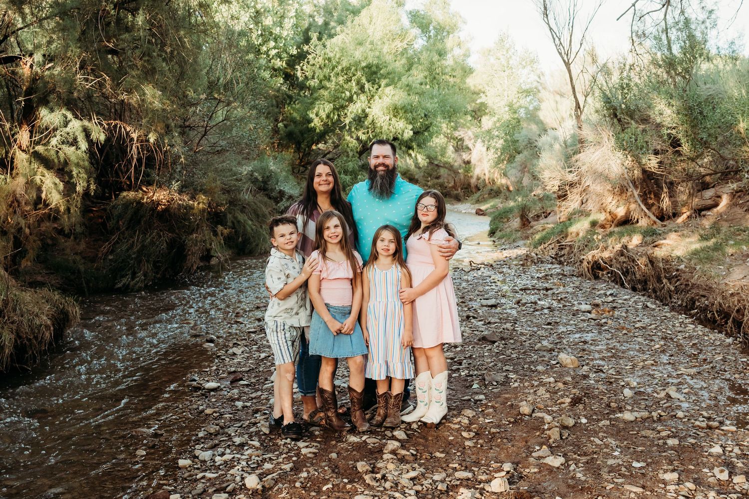 Bearded father and brunette mother posing with four young daughters by a rocky creek in nature.