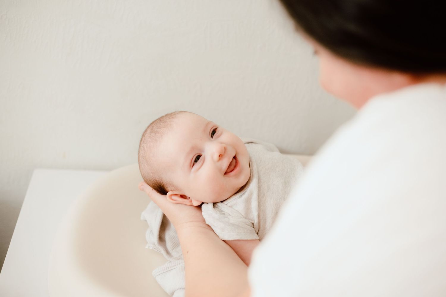Smiling newborn baby being held by mother in bright white nursery room.