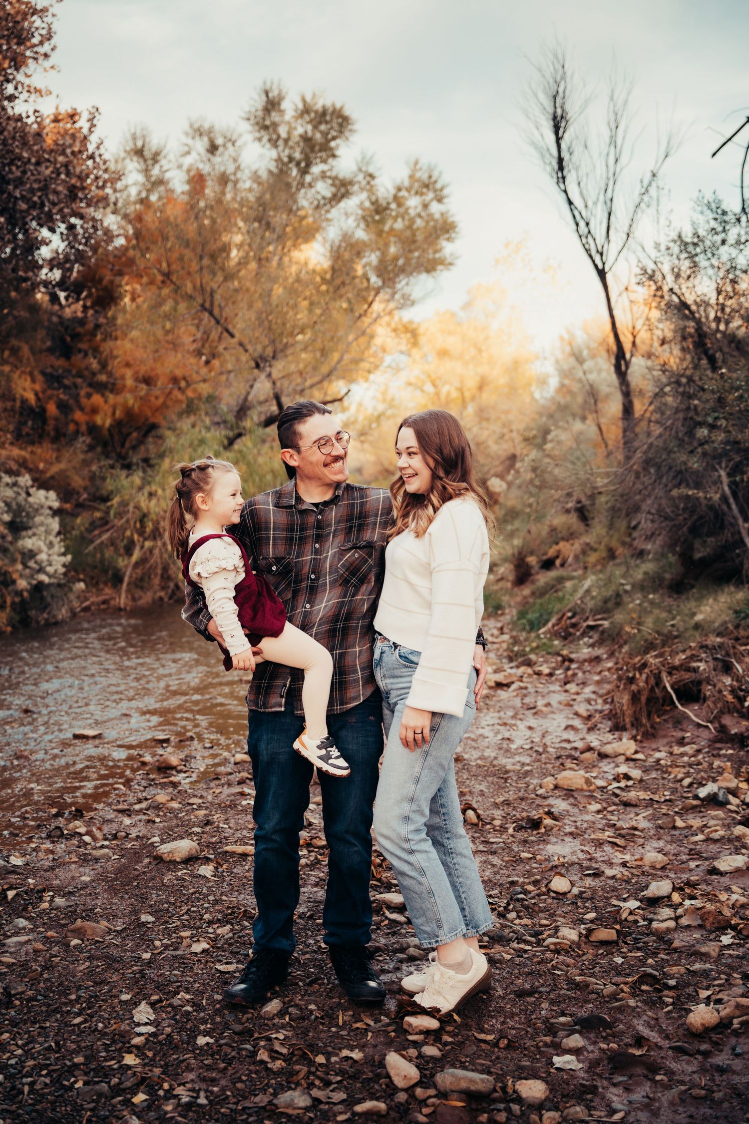 Smiling family with toddler sharing a joyful moment by a sunlit autumn creek.