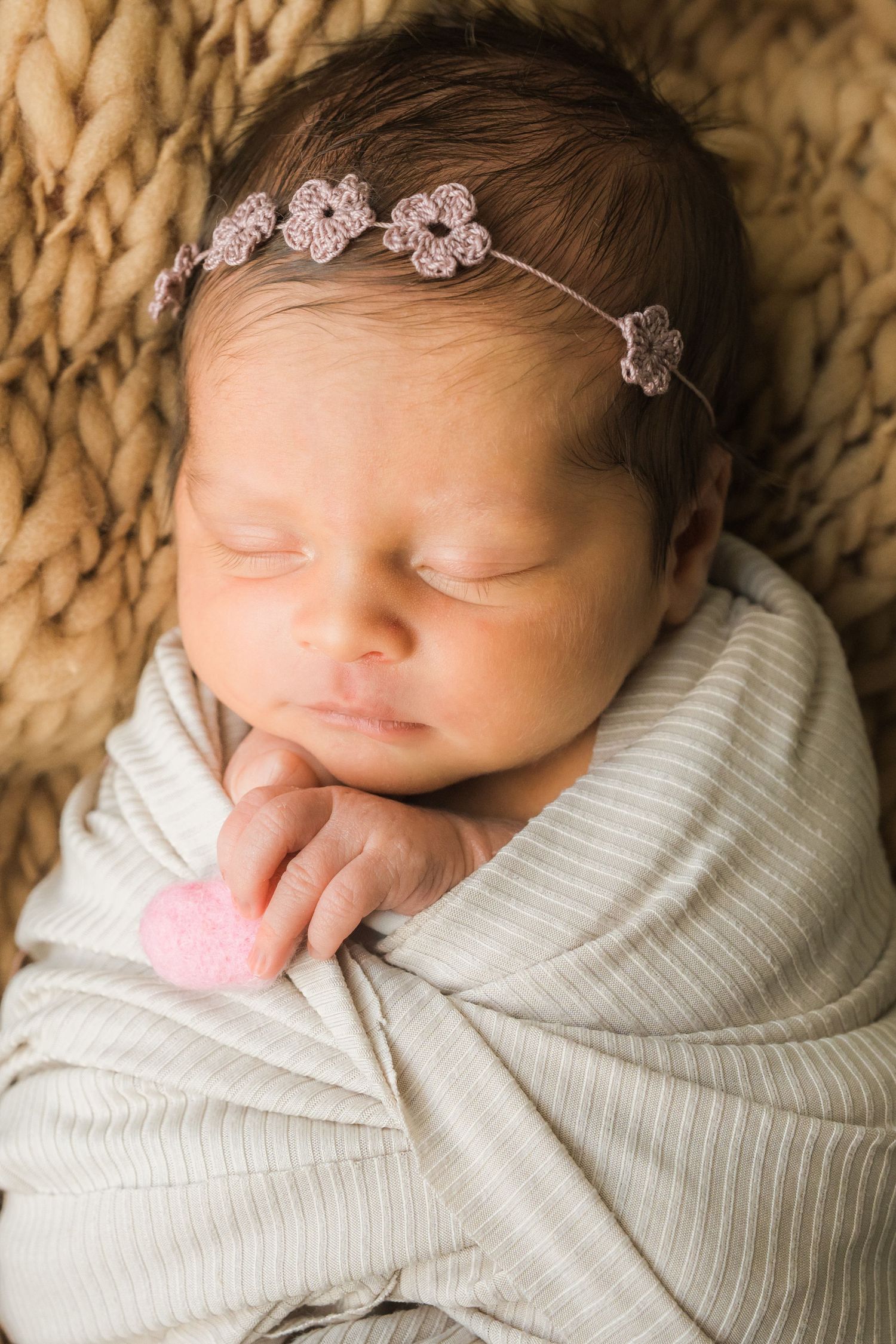 Close-up portrait of sleeping newborn baby wearing striped swaddle and delicate floral headband.