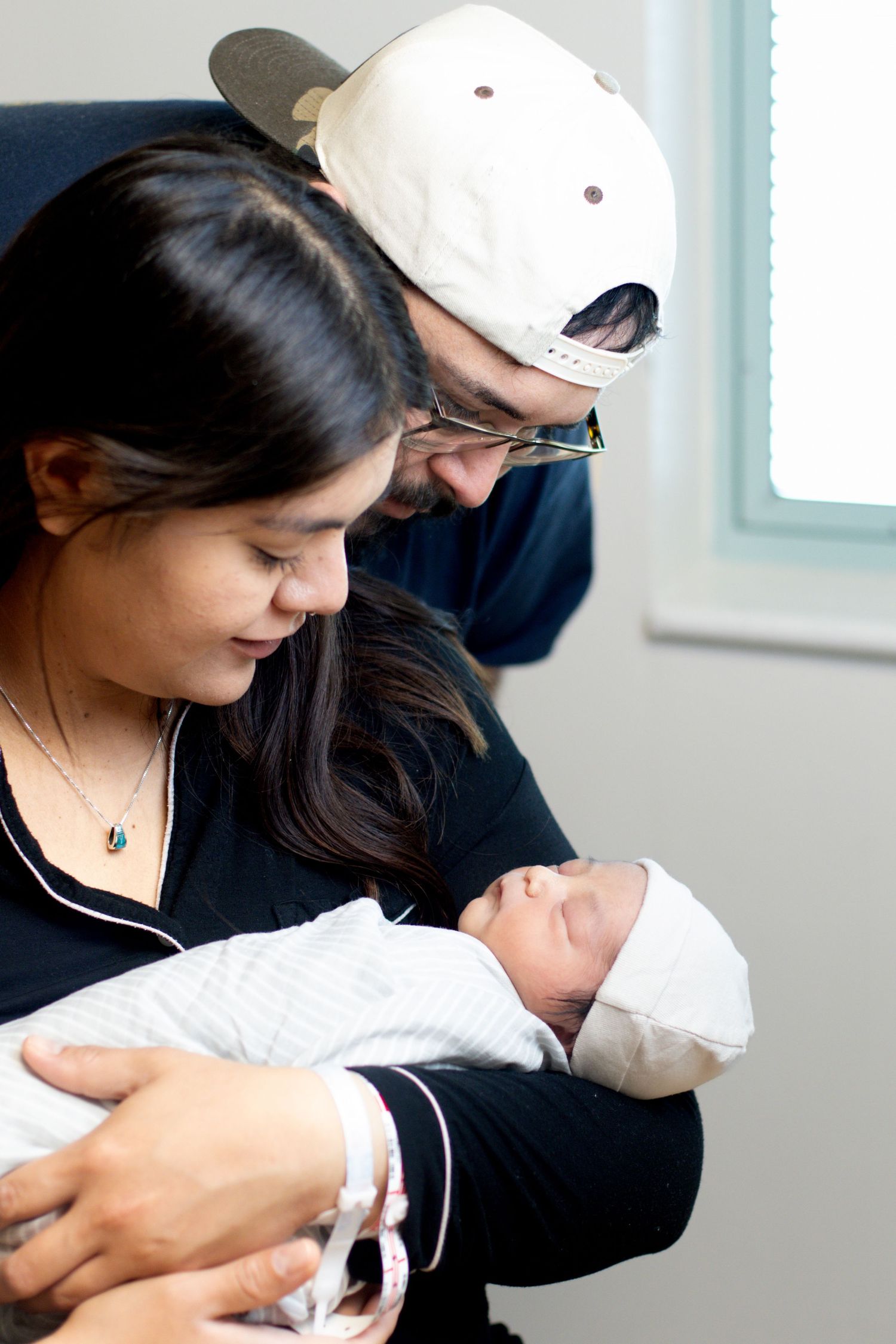 Happy new parents smiling and gazing lovingly at their swaddled newborn baby in hospital.