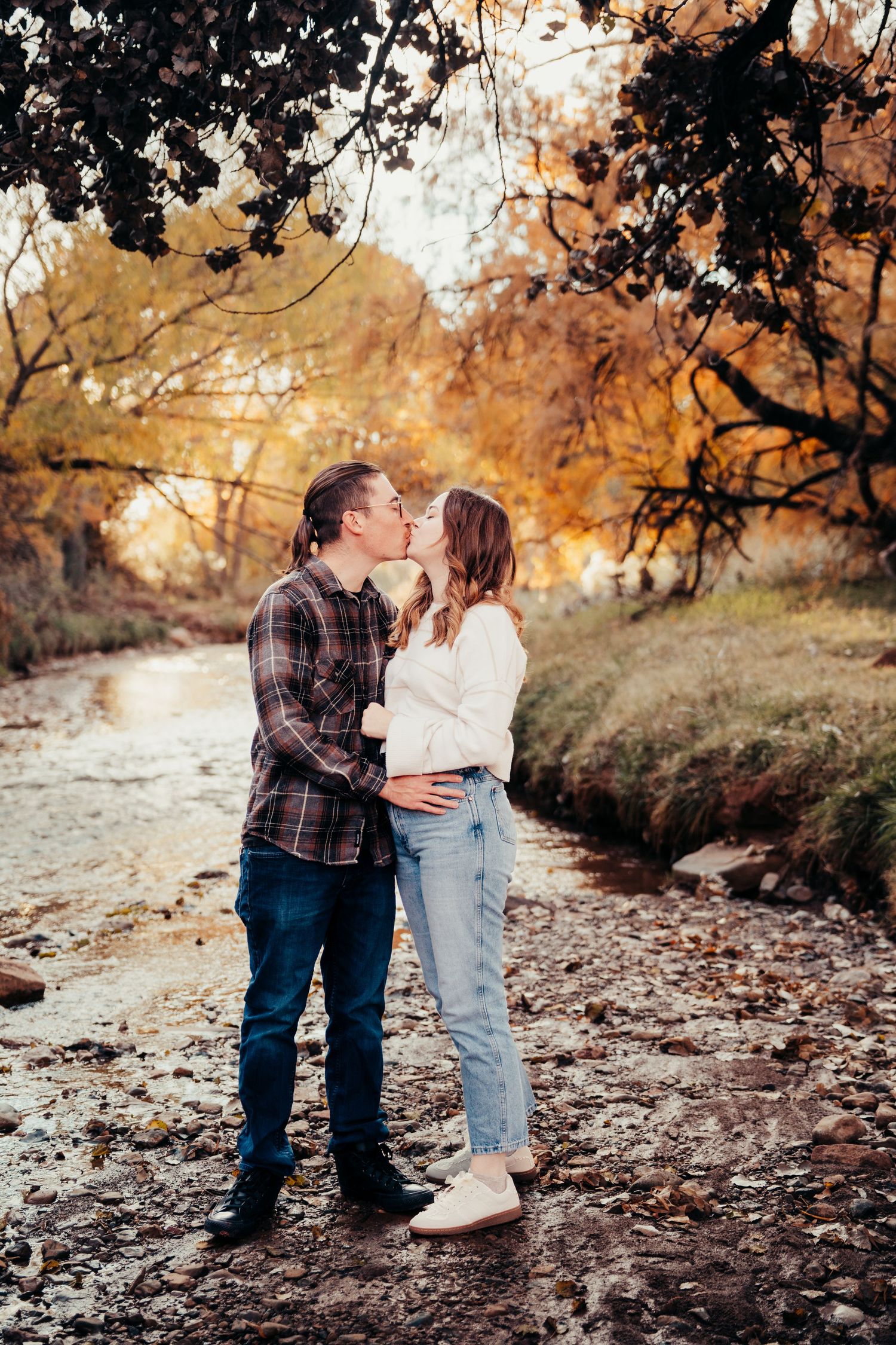 Couple sharing a kiss beside a rocky creek in an autumn forest setting.