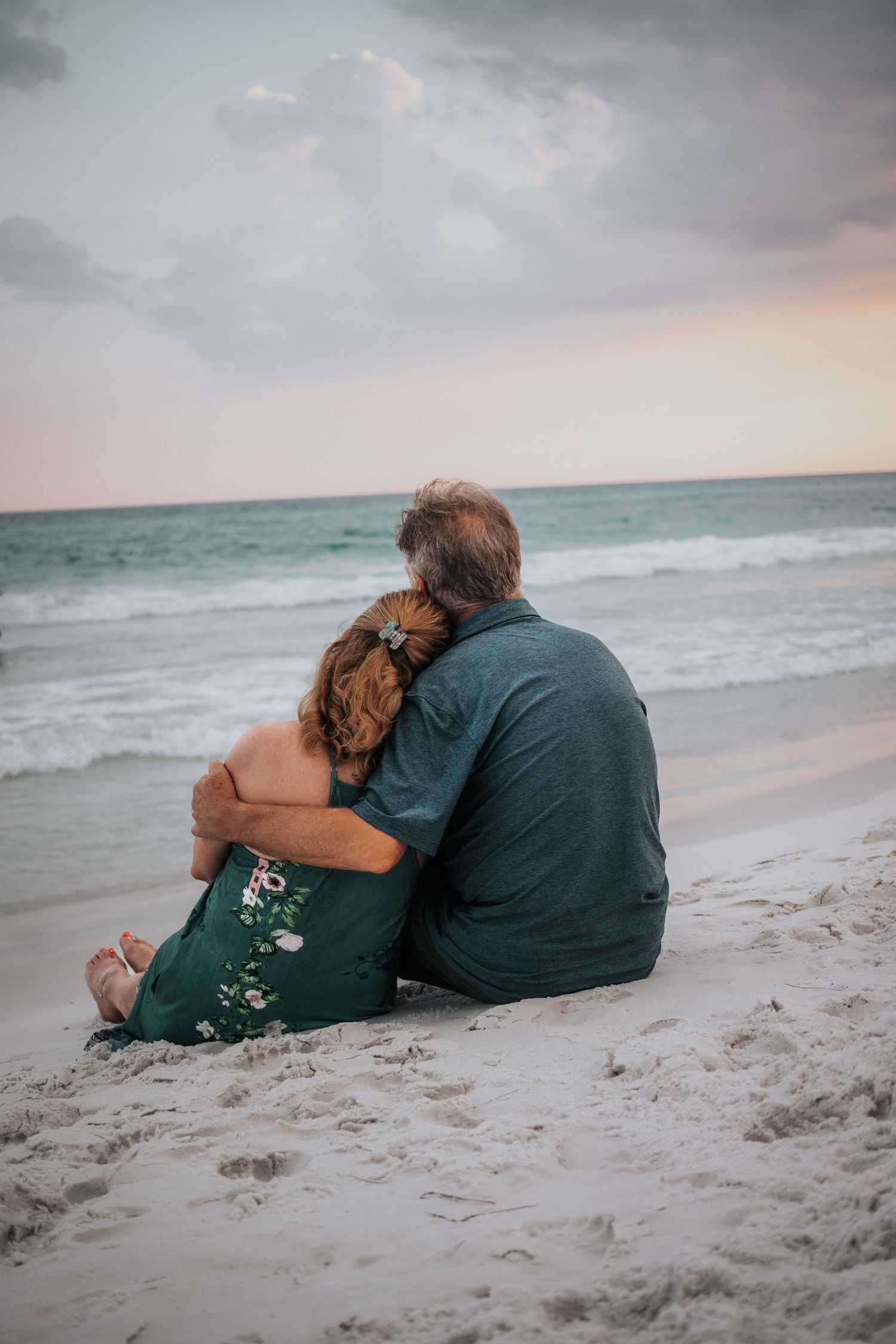 Couple sitting together on the sand facing the ocean waves at a peaceful beach sunset.