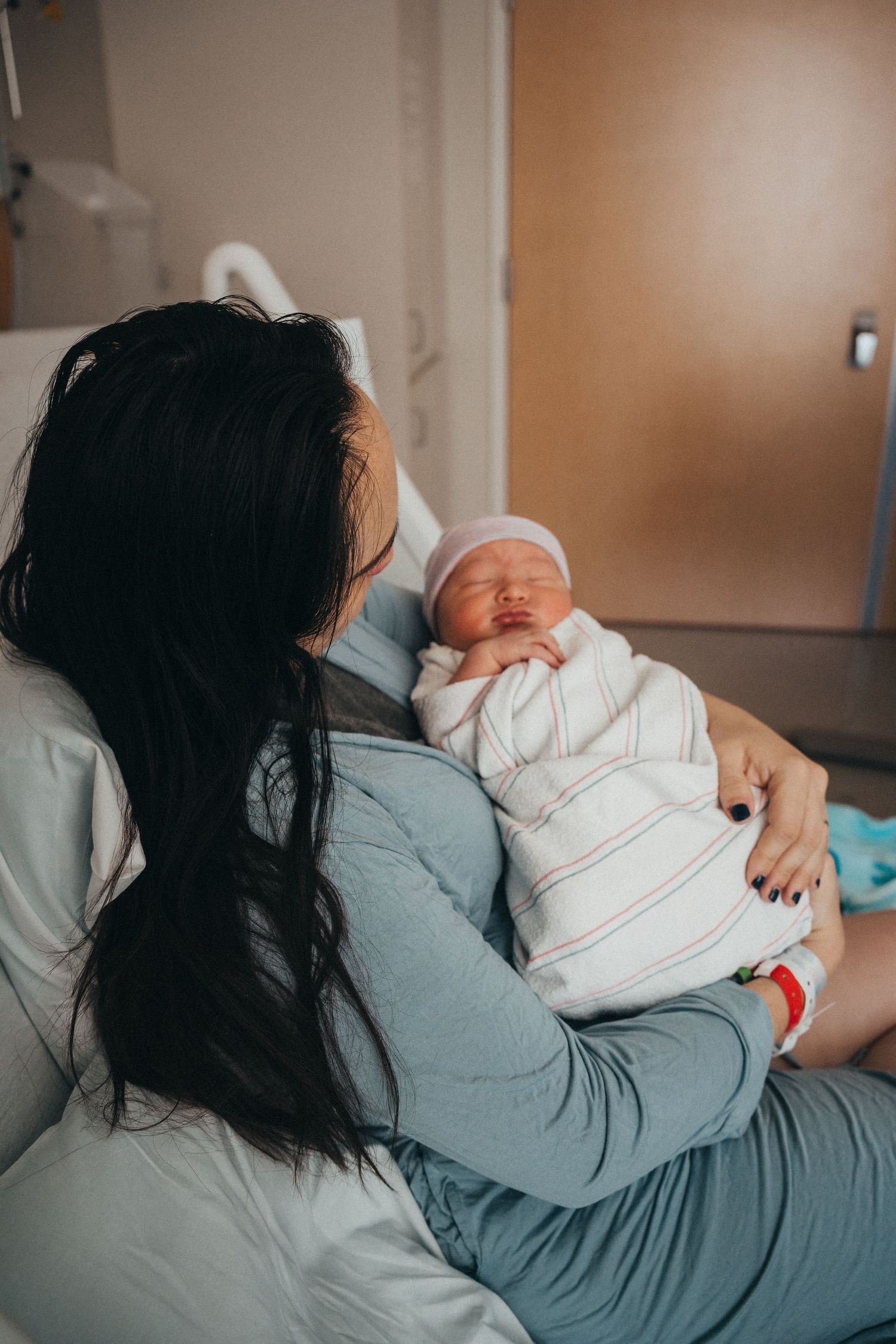 A new mother with long dark hair holds her swaddled newborn baby in a hospital room after giving birth.