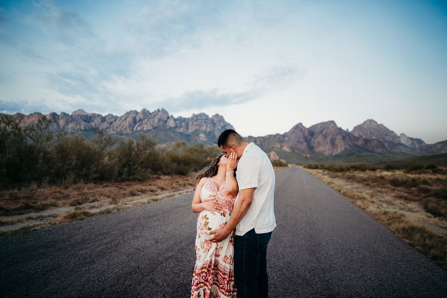 Expecting couple embracing lovingly on a scenic road with stunning Organ Mountains behind them.