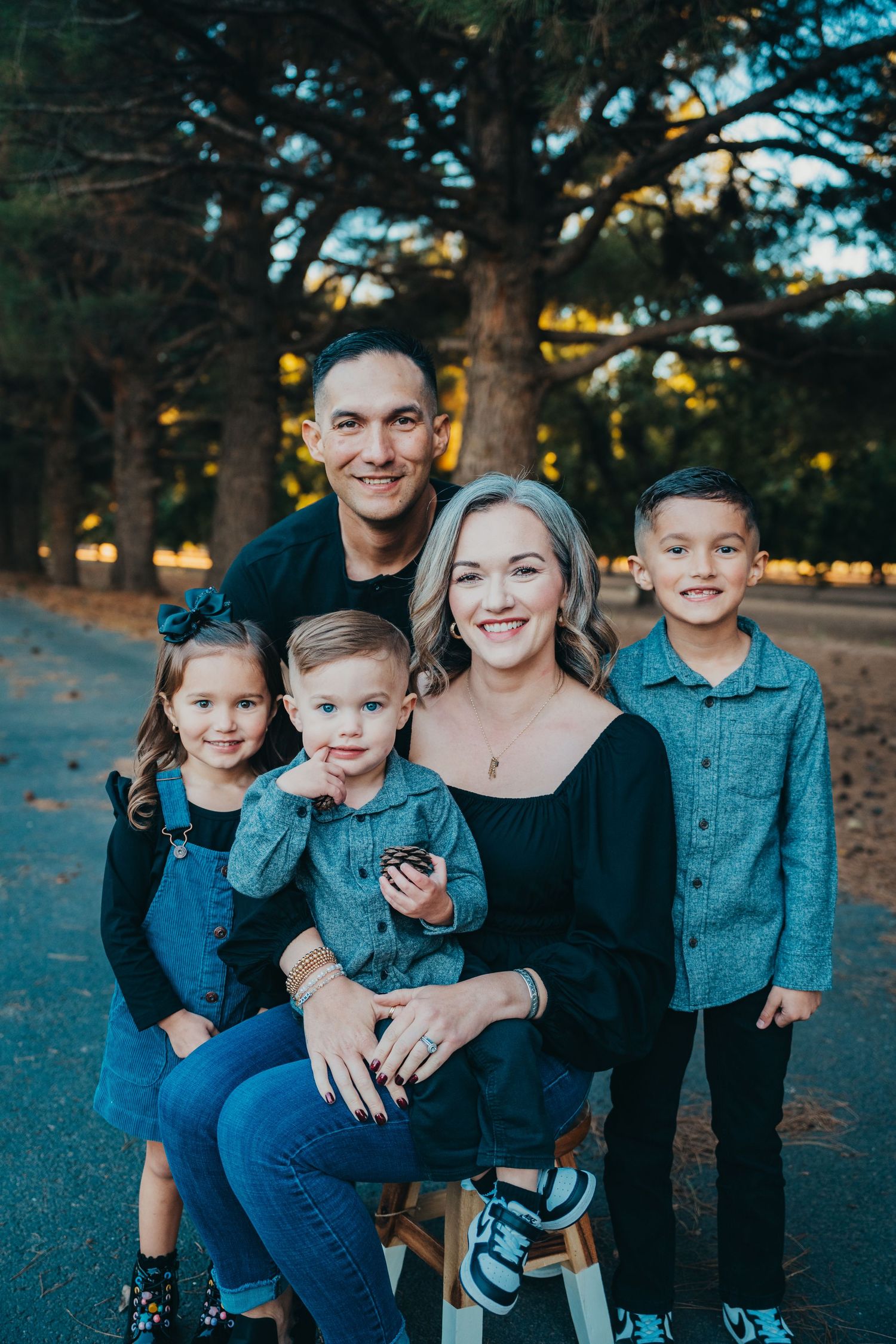 Happy family of five posing outdoors in a park during golden hour, parents with three young children in coordinating blue outfits.