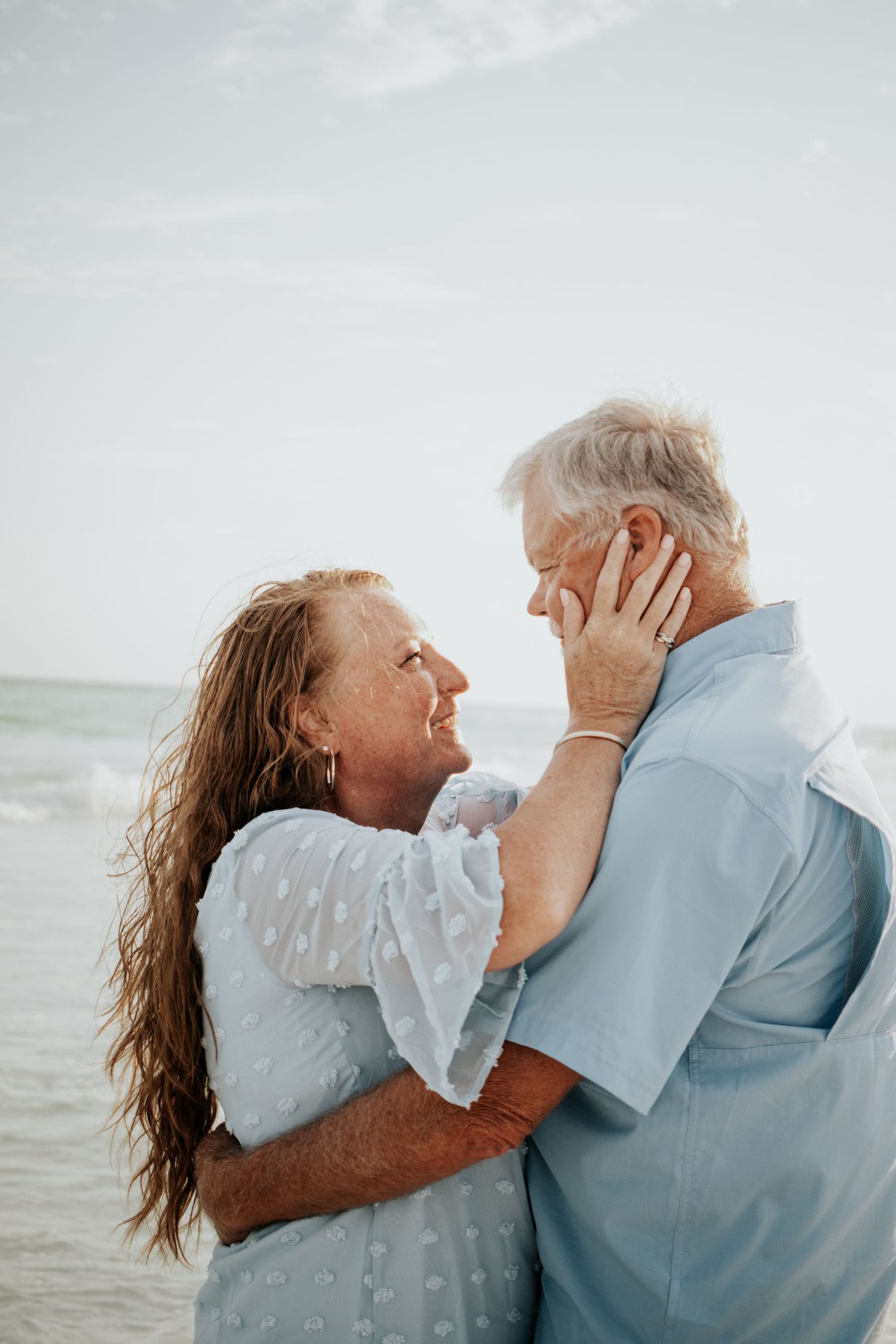 Mature couple embracing on beach, woman tenderly holding mans face while gazing into each others eyes.