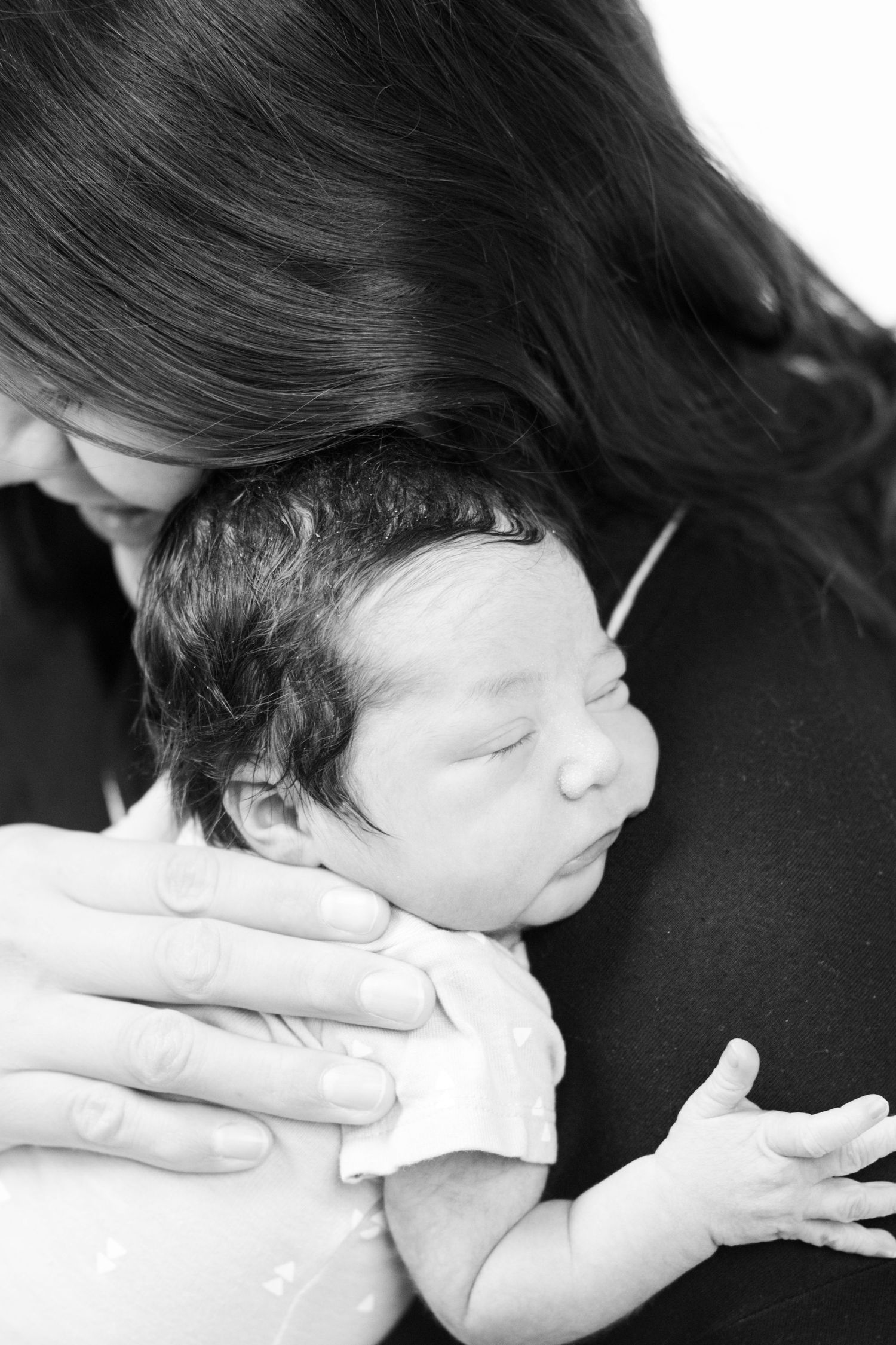 Black and white photo of a mother tenderly cradling her sleeping newborn baby close to her chest.