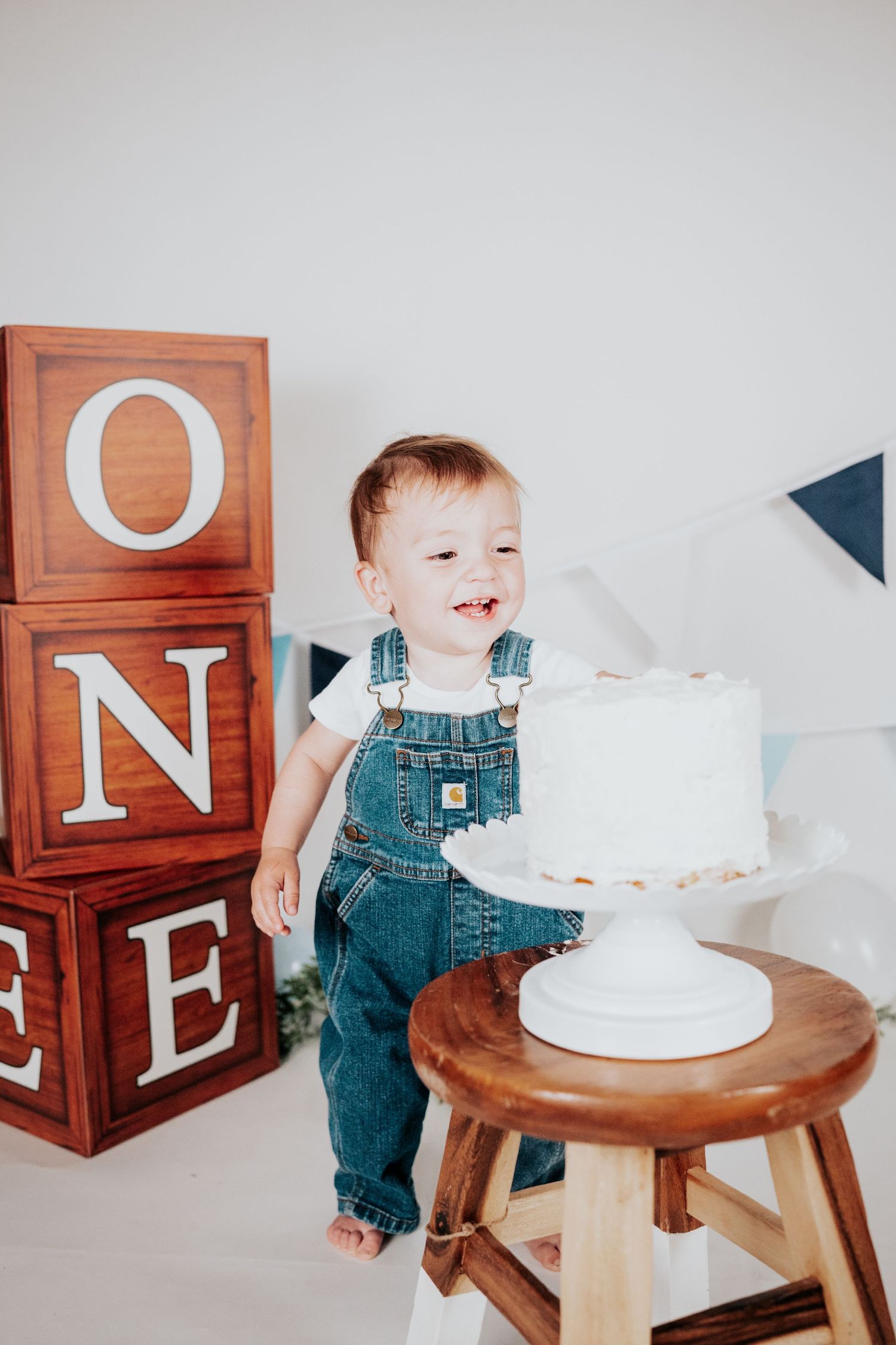 Happy one-year-old in Carhartt denim overalls laughing beside first birthday smash cake.