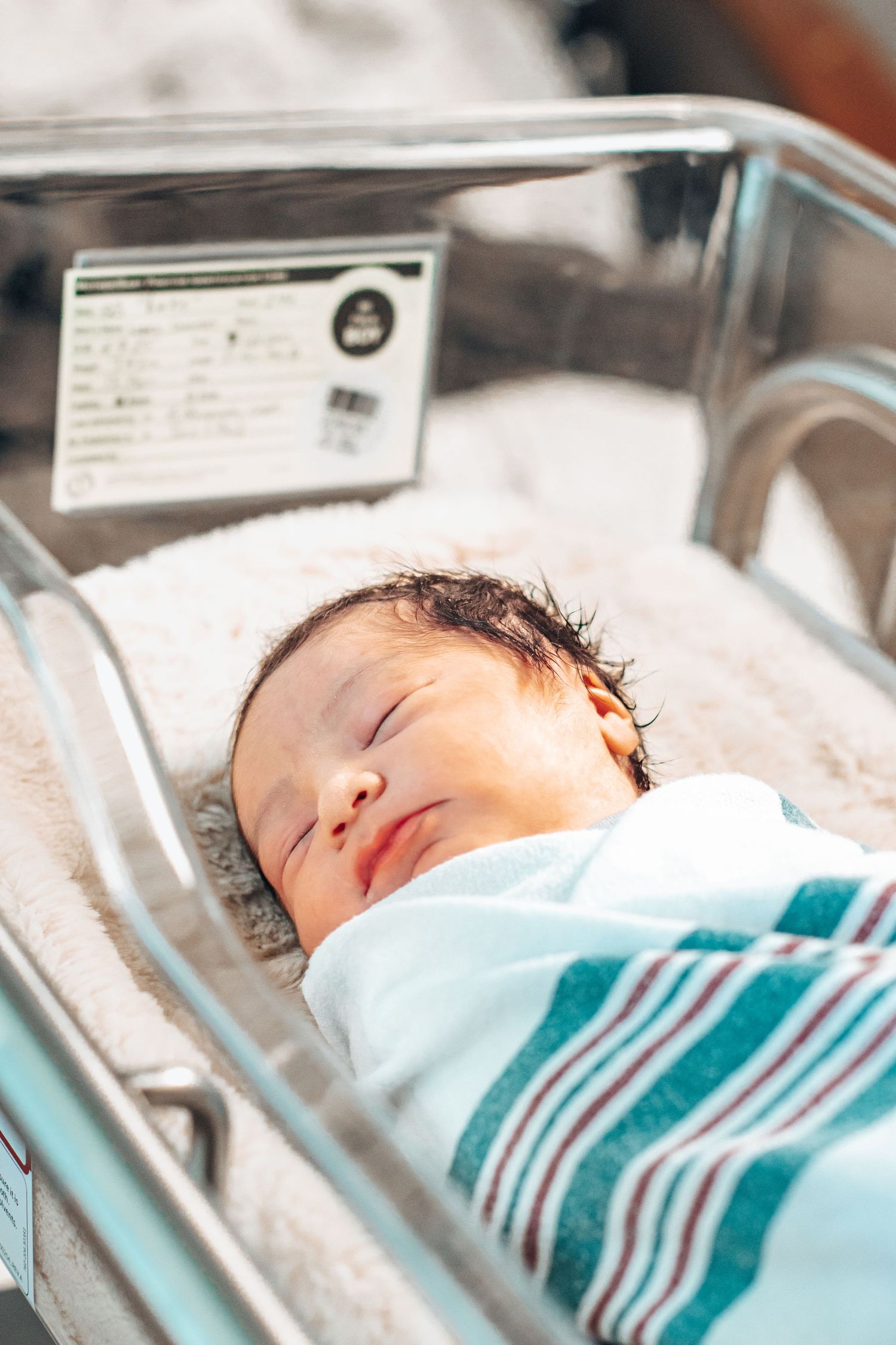Peaceful newborn baby sleeping swaddled in striped blanket inside hospital bassinet after birth.