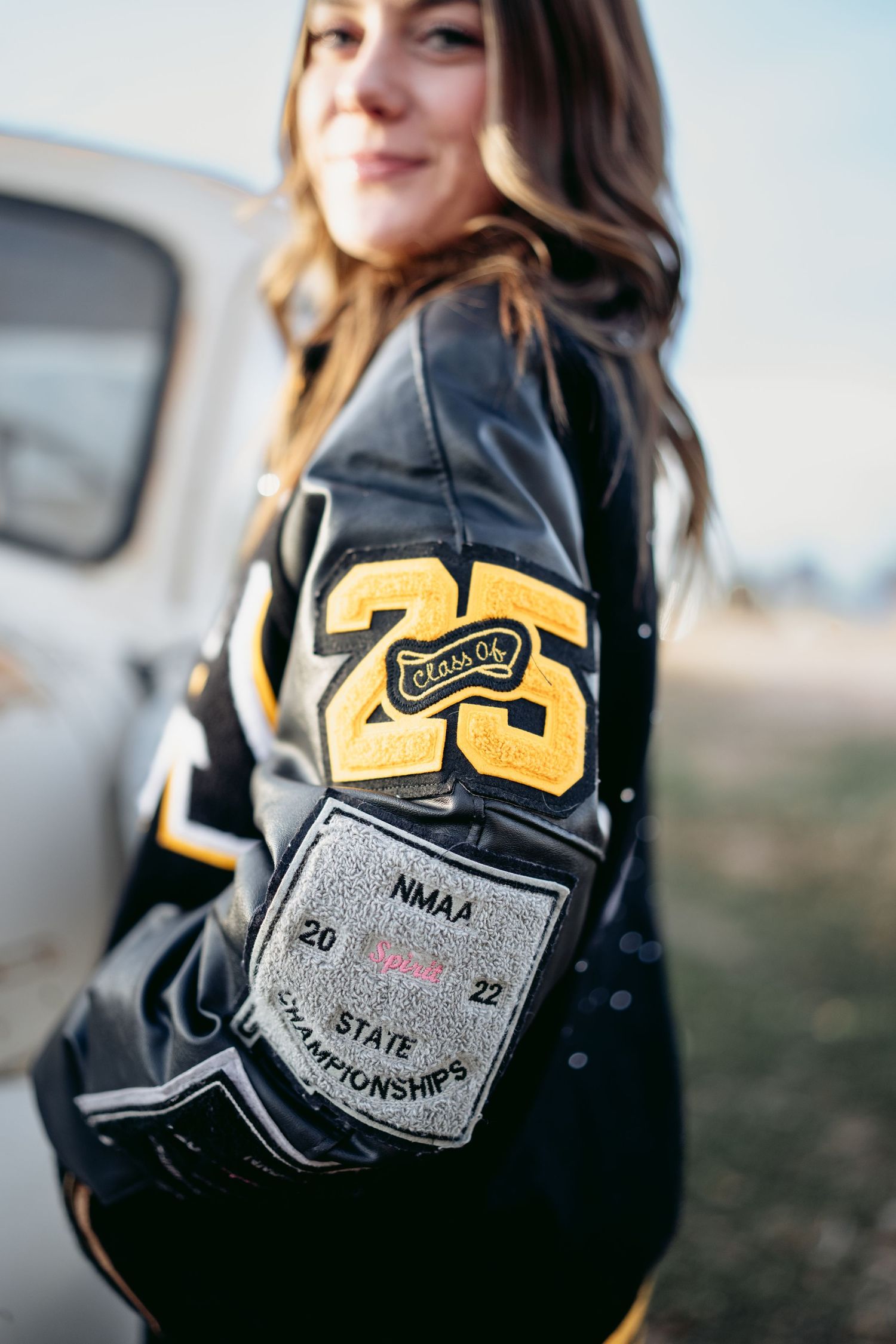 Close-up of a black and gold letterman jacket with Class of 25 patch and NMAA State Championships patch.