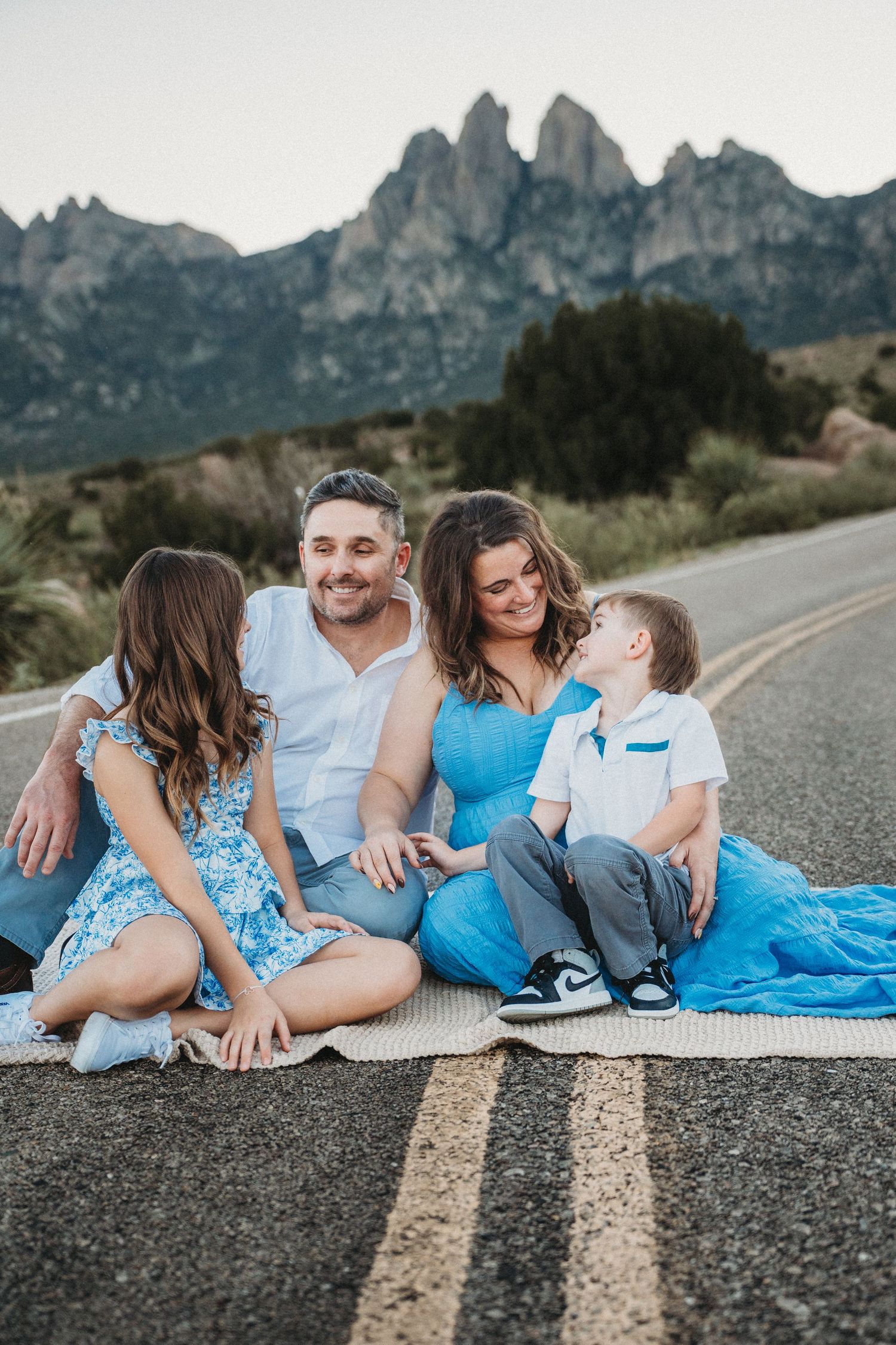 Candid family photo of four sitting on a mountain road, laughing and interacting in blue and white.