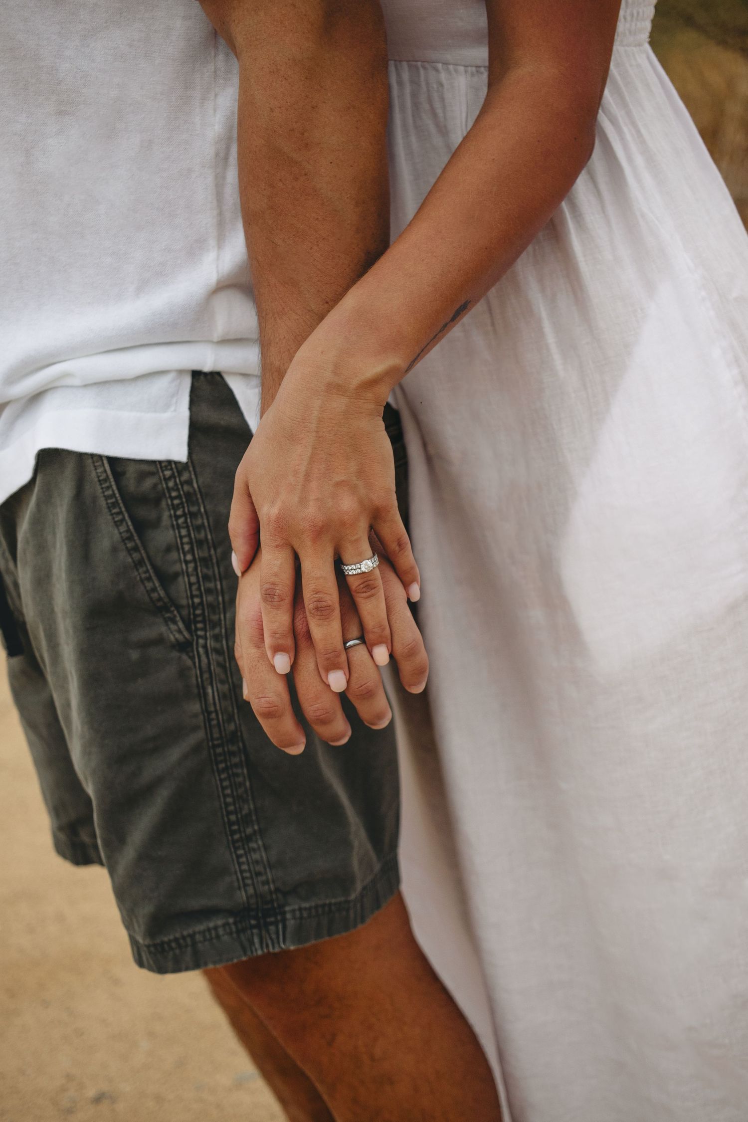 Close-up of couple holding hands showing engagement ring in outdoor desert setting.