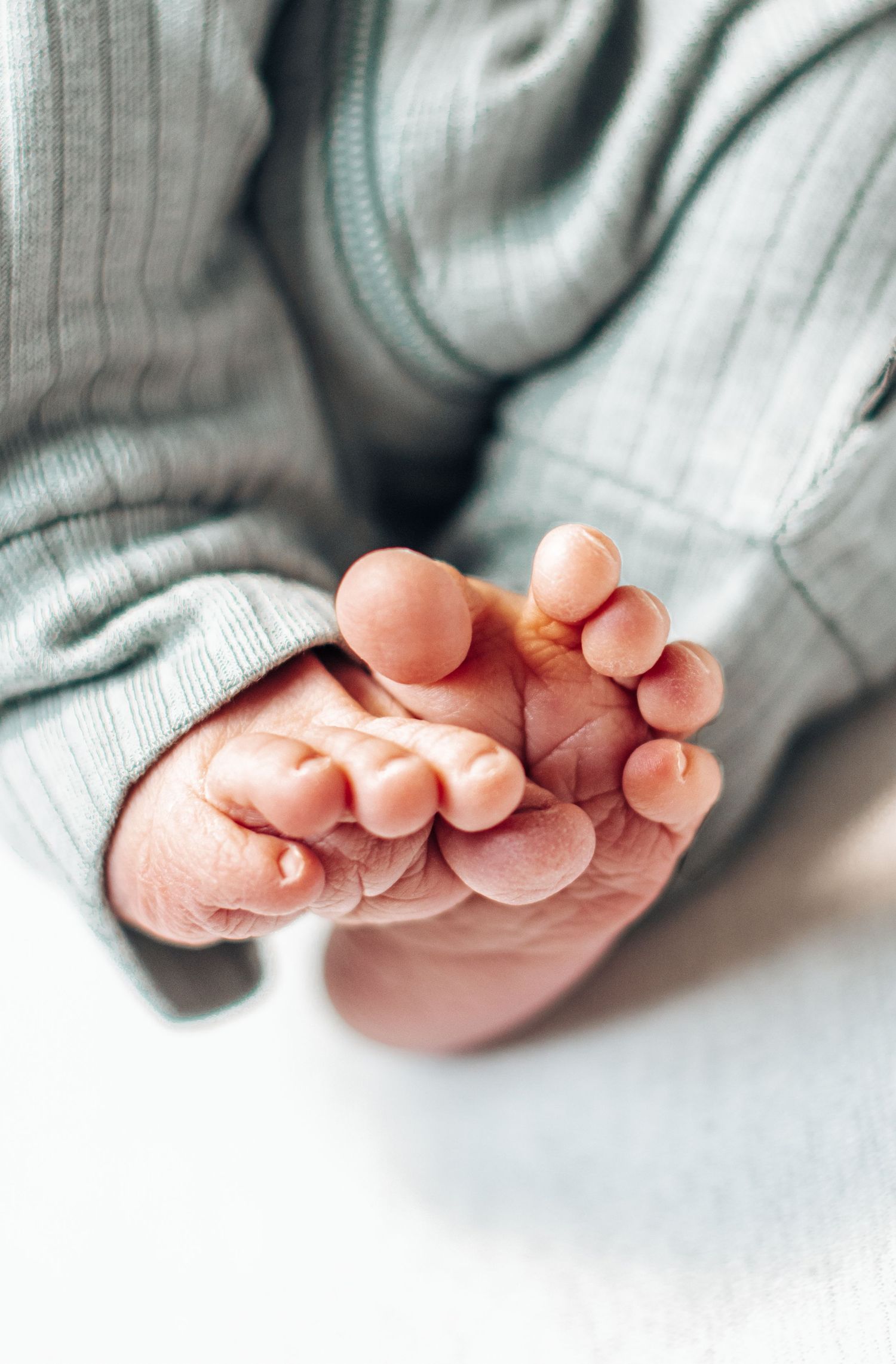 Extreme close-up of tiny newborn baby feet and toes in soft green ribbed onesie.