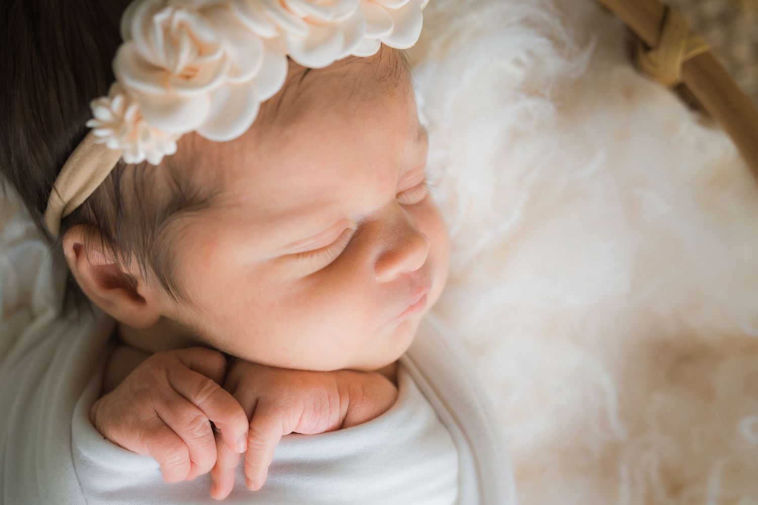 Close-up of sleeping newborn baby girl in white wrap with cream floral headband.