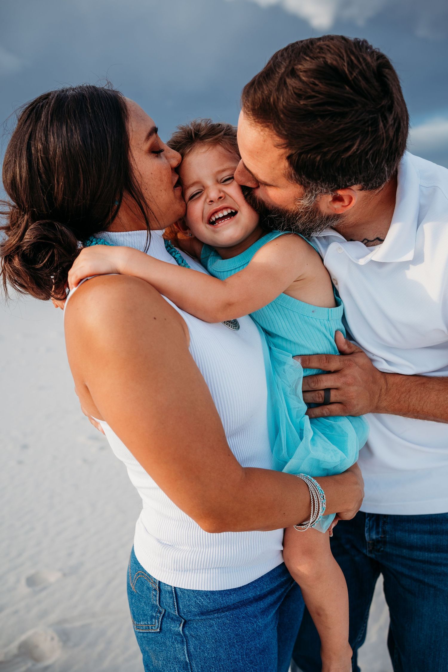 Two loving parents simultaneously kiss their laughing young daughter on the cheeks at White Sands.
