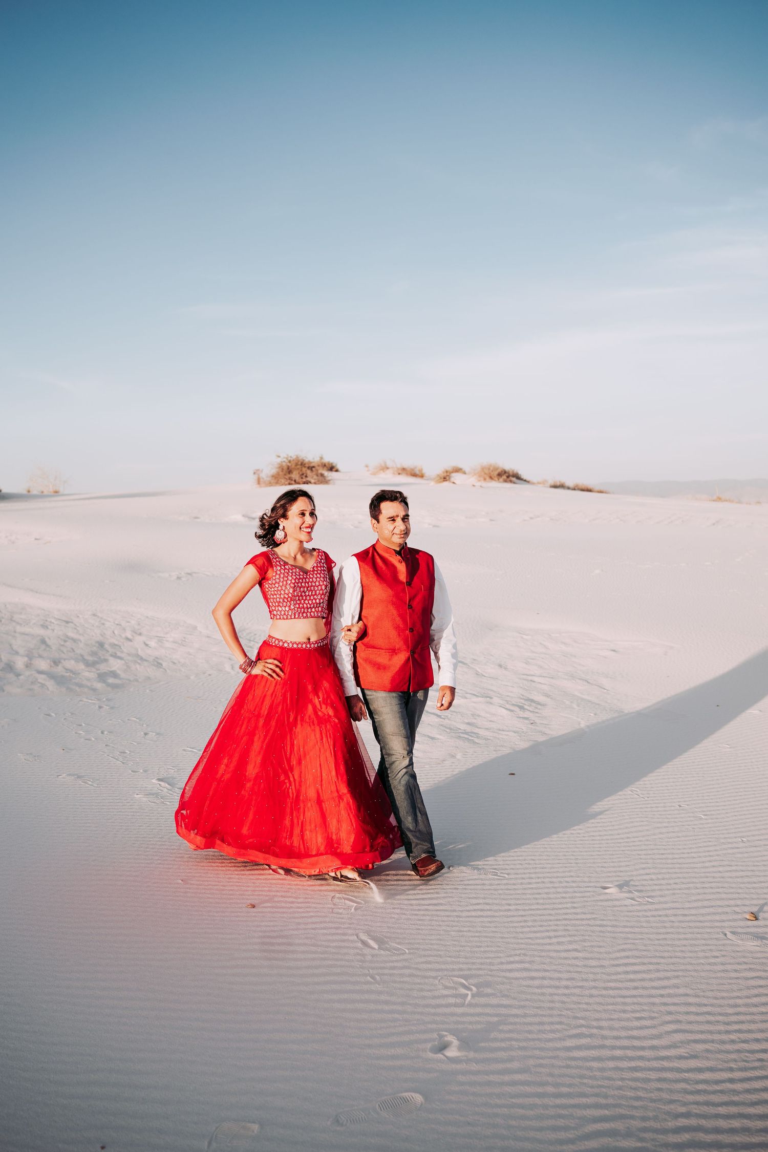 Couple dressed in red Indian traditional clothing strolling together on expansive white sand dunes.
