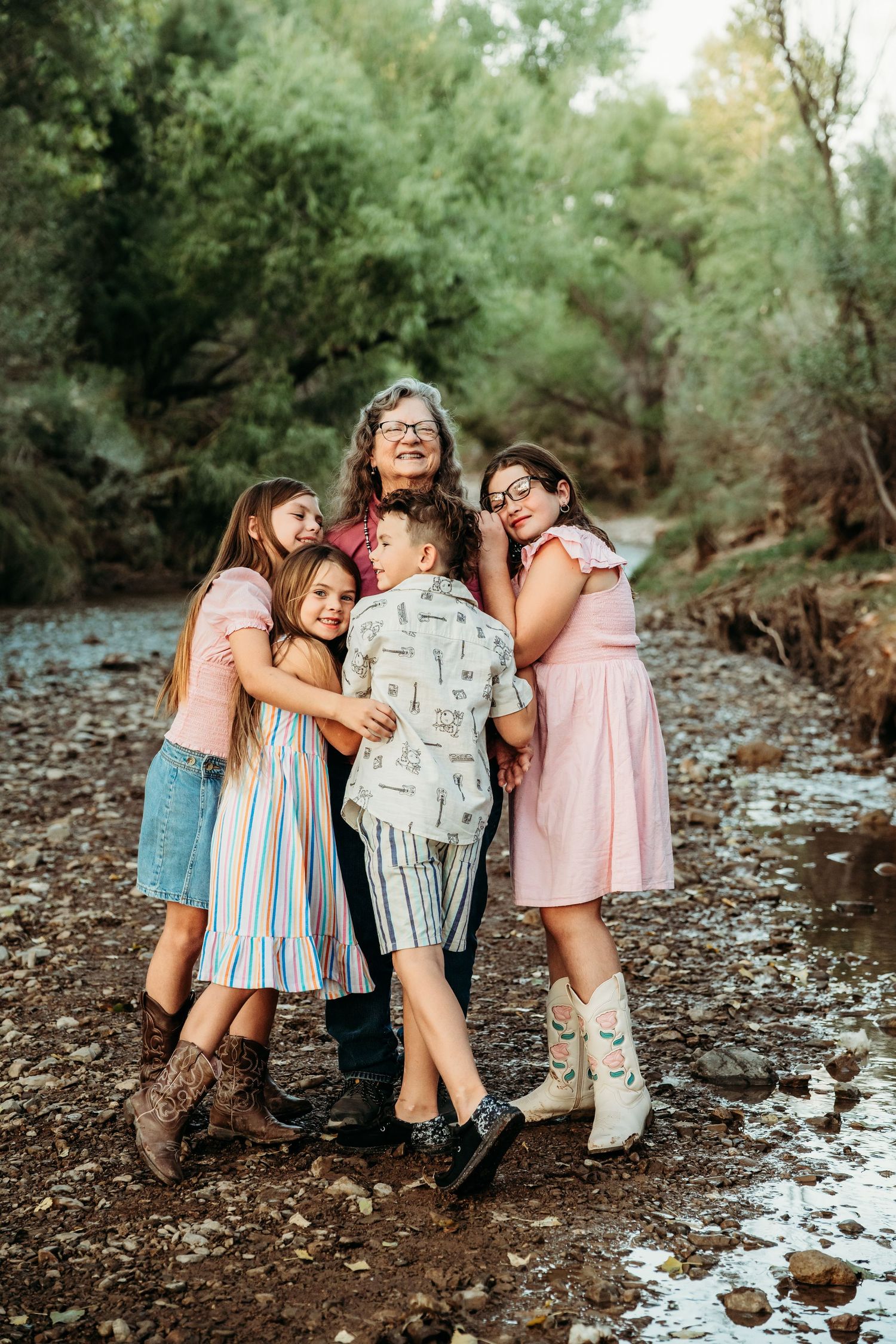 Grandmother shares a warm group hug with four grandchildren outdoors by a creek.