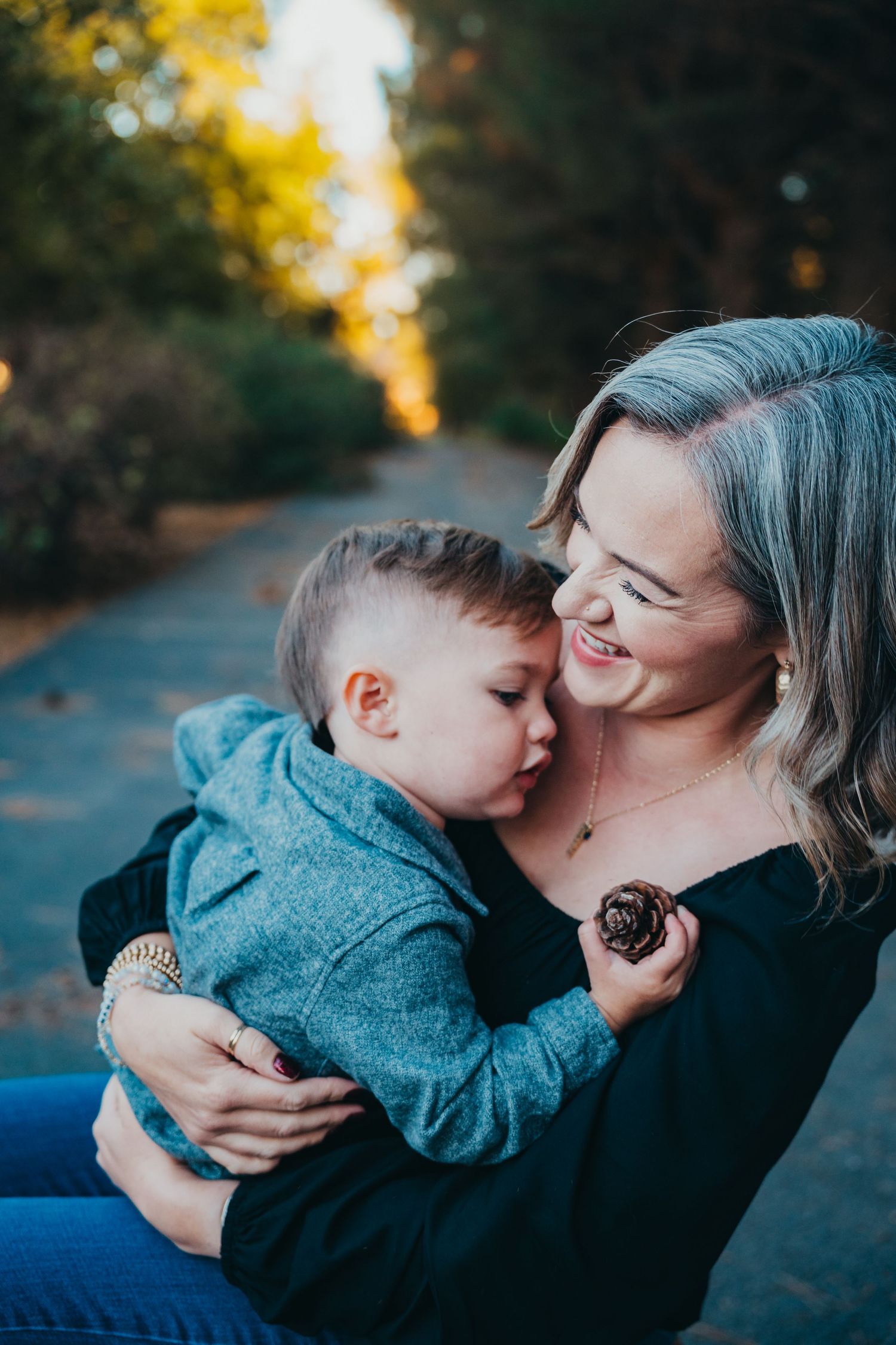 A joyful toddler giving his laughing mother a kiss on the cheek while being held outdoors in a park.