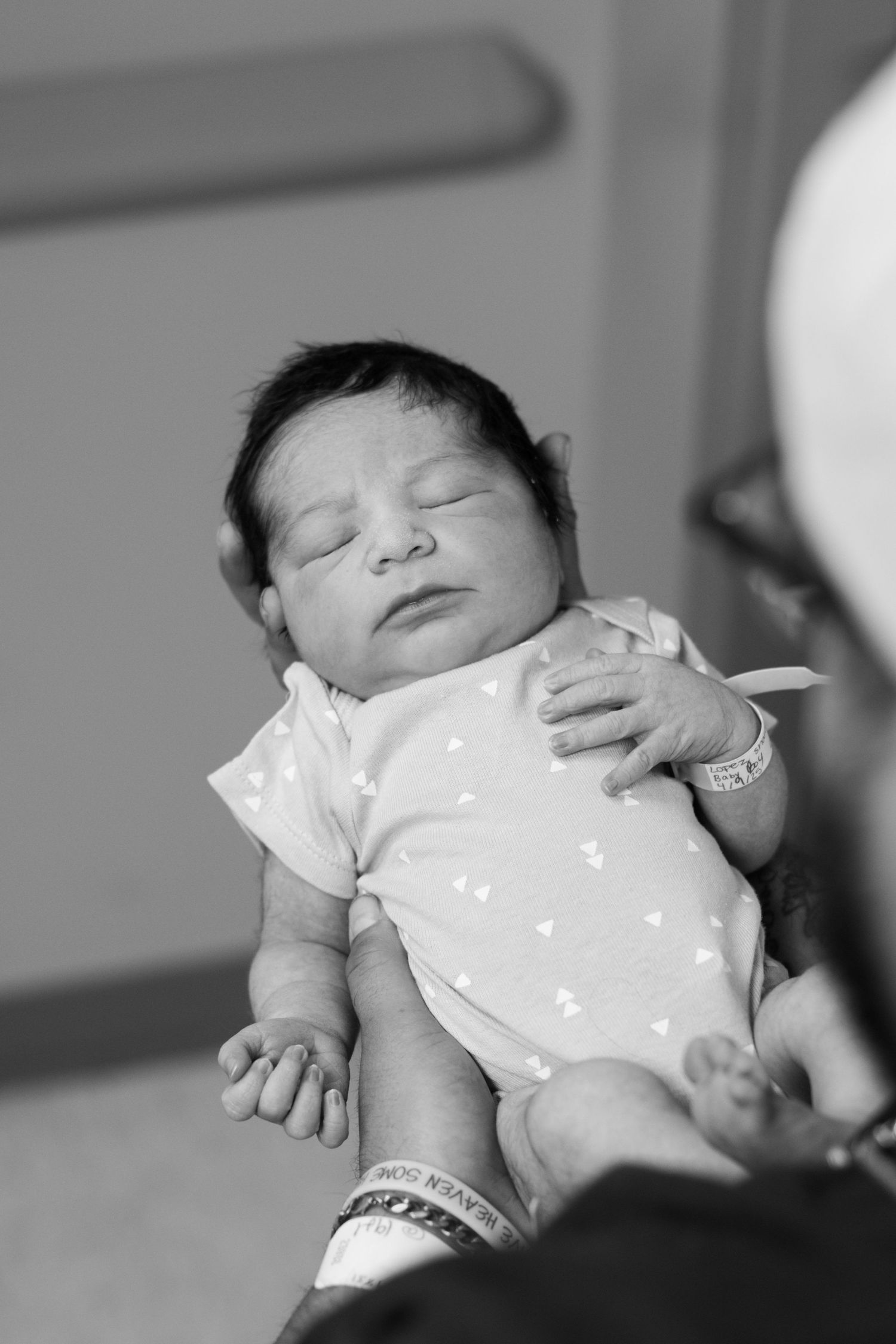 Black and white photo of sleeping newborn baby in hospital onesie.