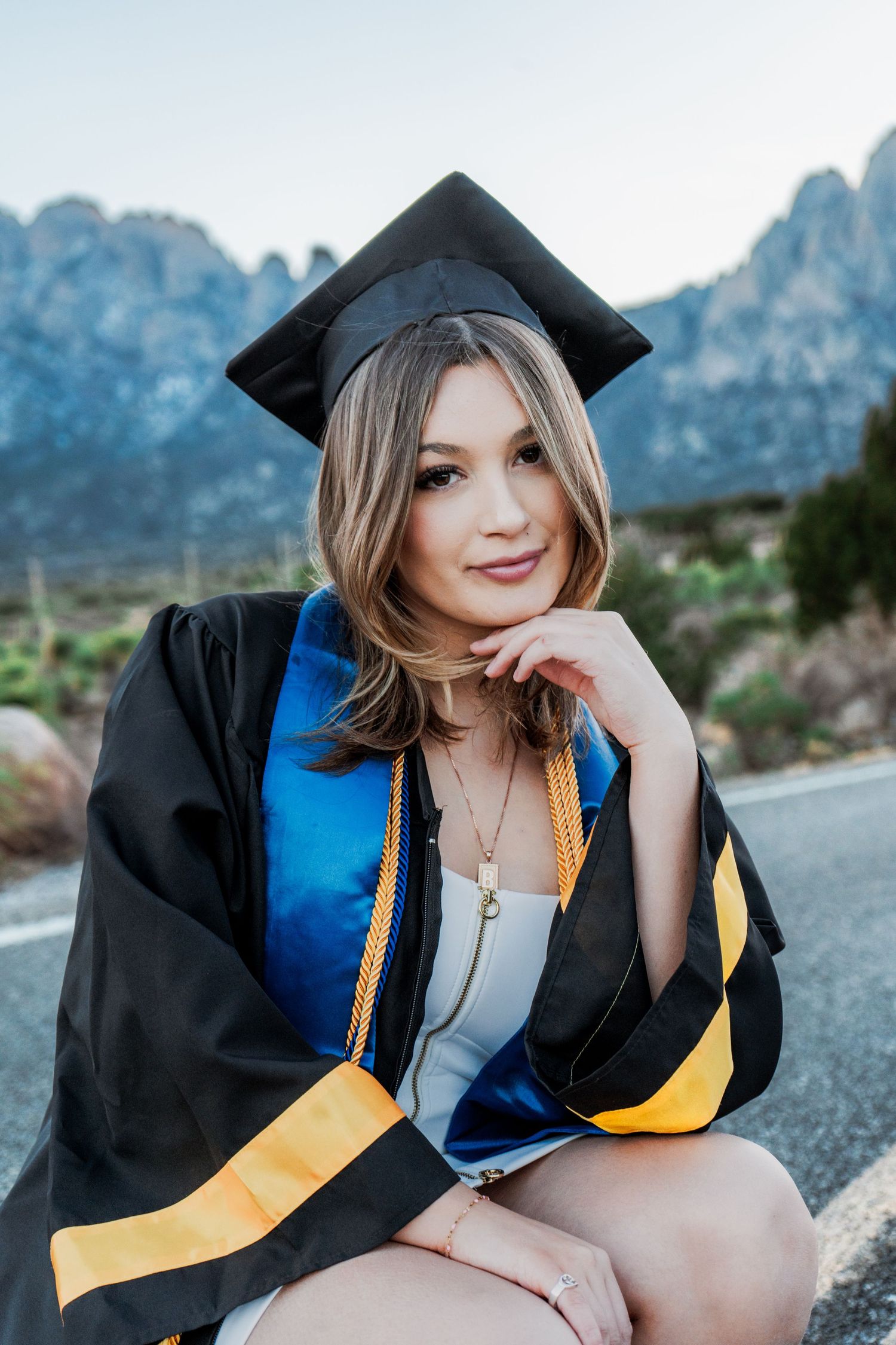 Close-up portrait of a smiling graduate in black cap and gown with blue and gold stole.