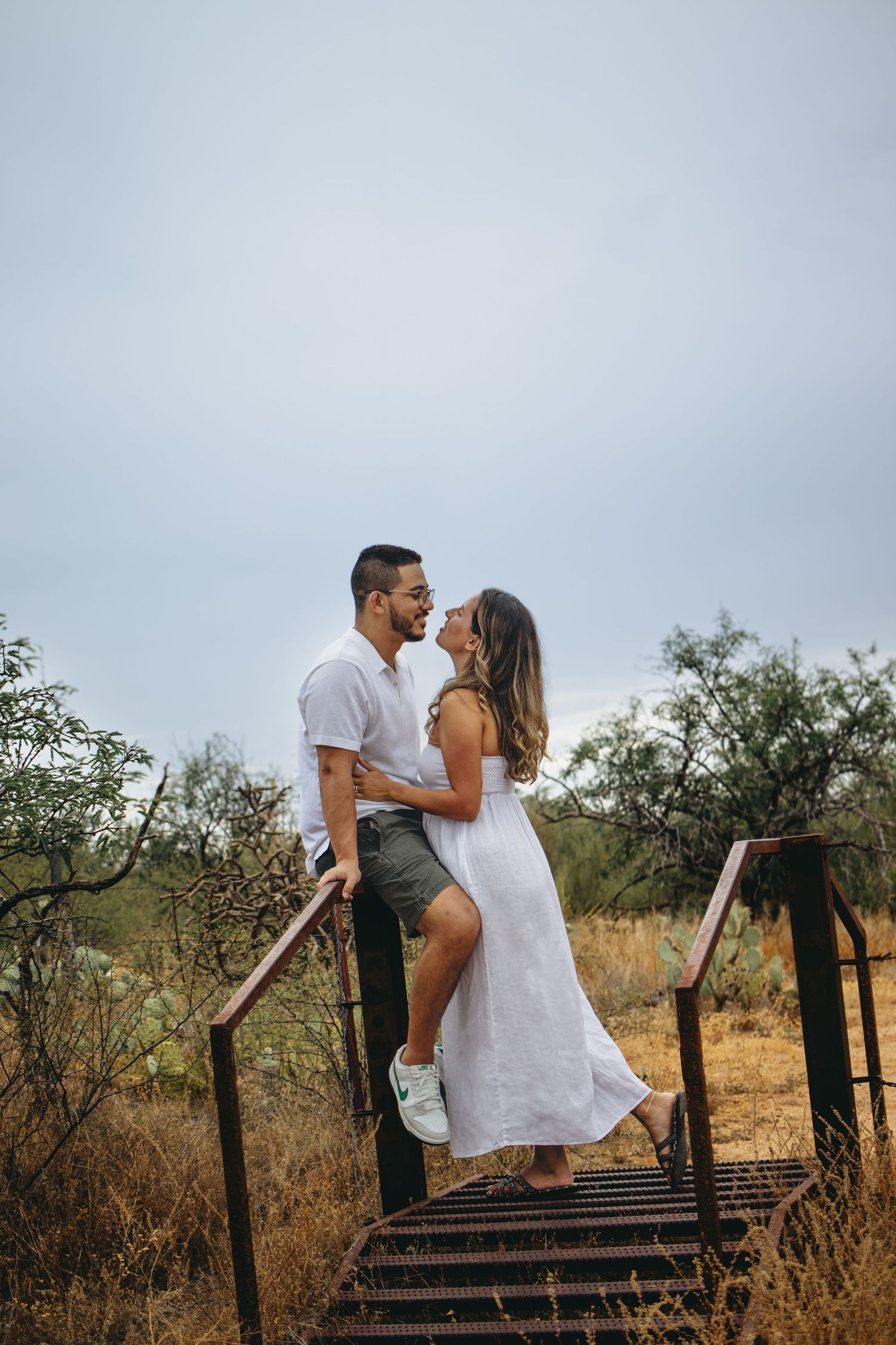 Romantic couple sharing a kiss on rustic metal stairs surrounded by desert shrubs.