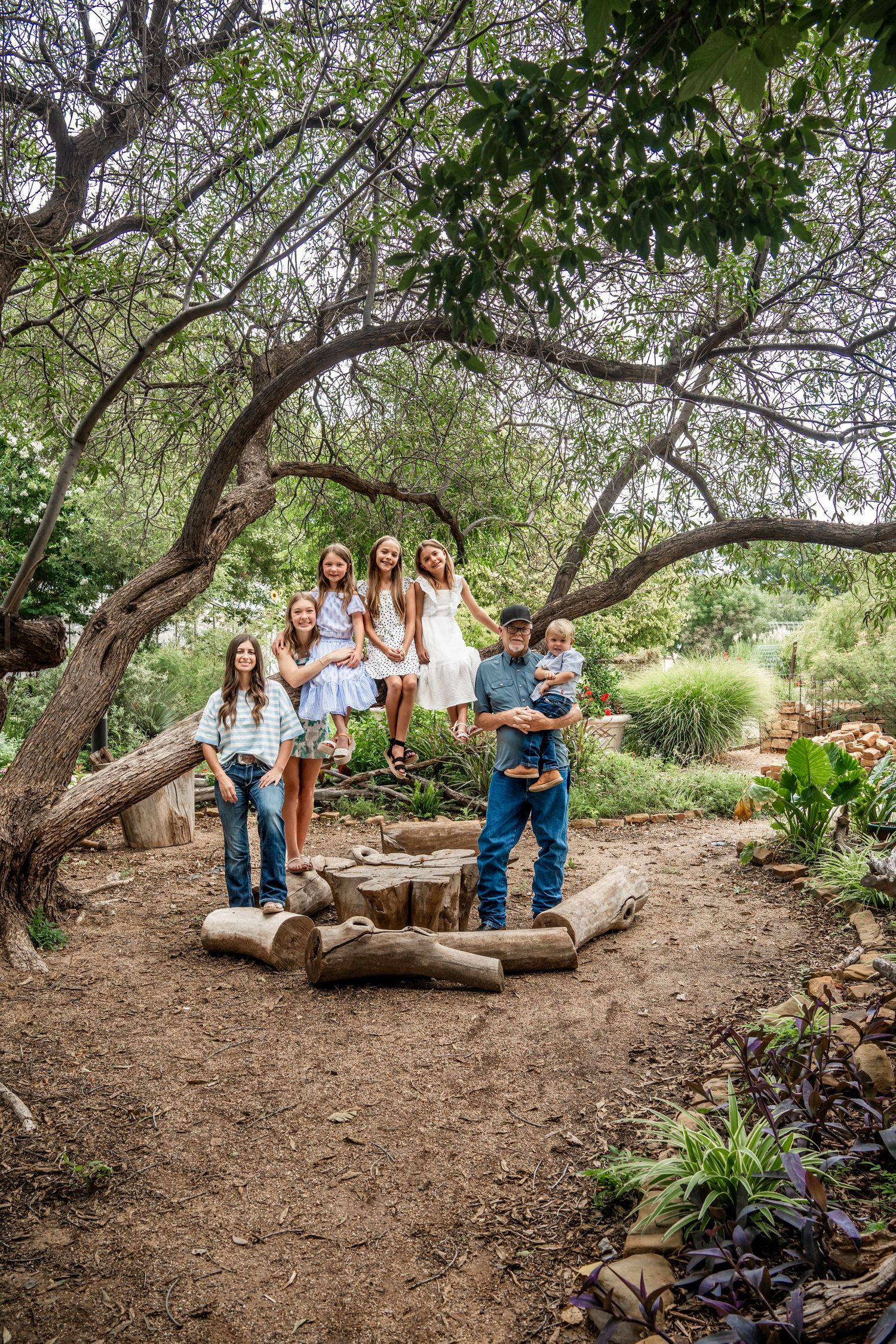 Family of seven posing creatively on logs and tree branches in rustic outdoor setting.