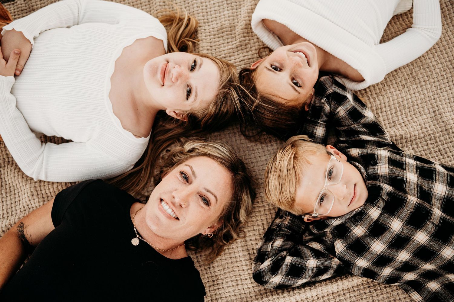 Overhead view of mother and three children lying together on blanket smiling.