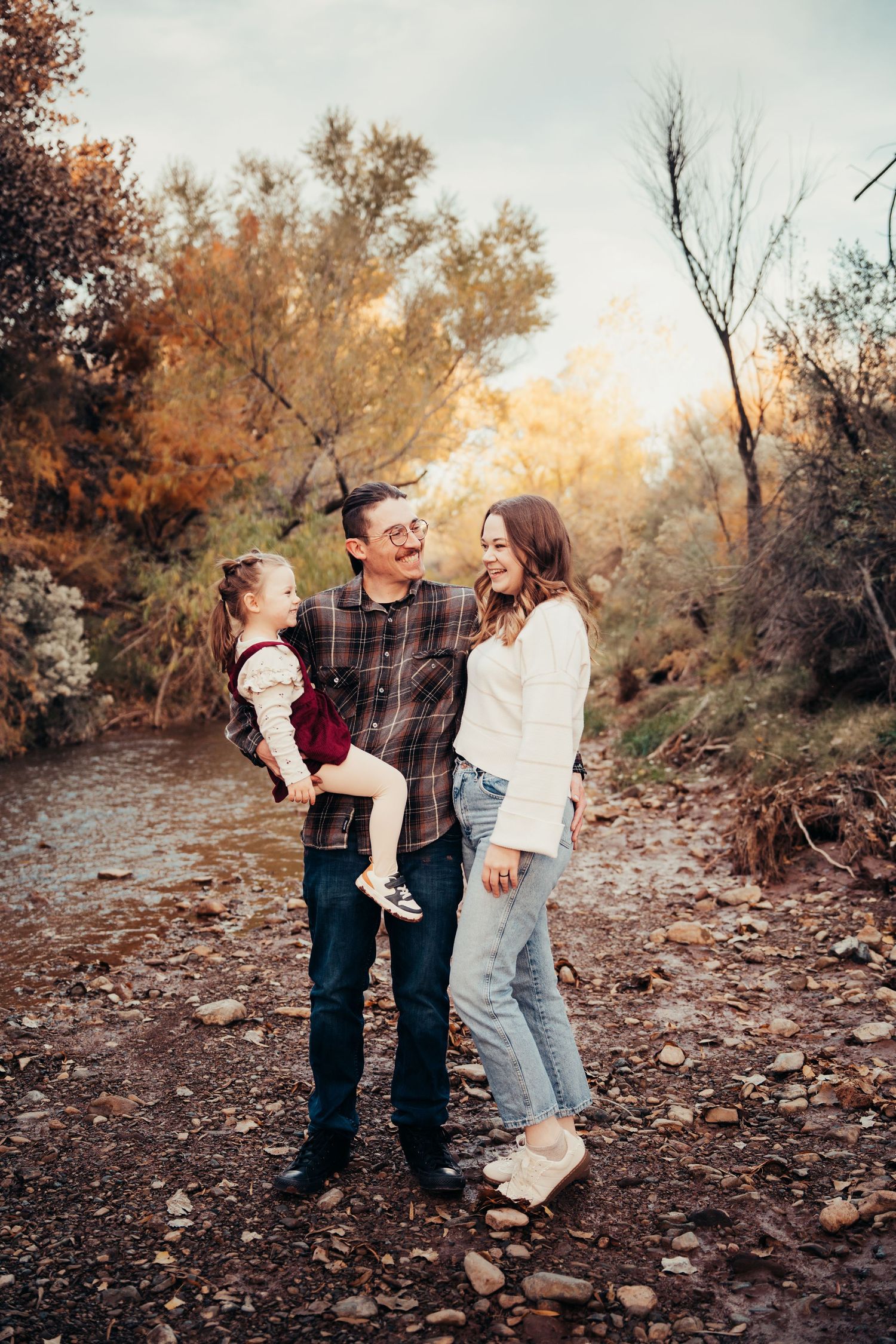 Happy family with young child laughing together near a stream in fall foliage.