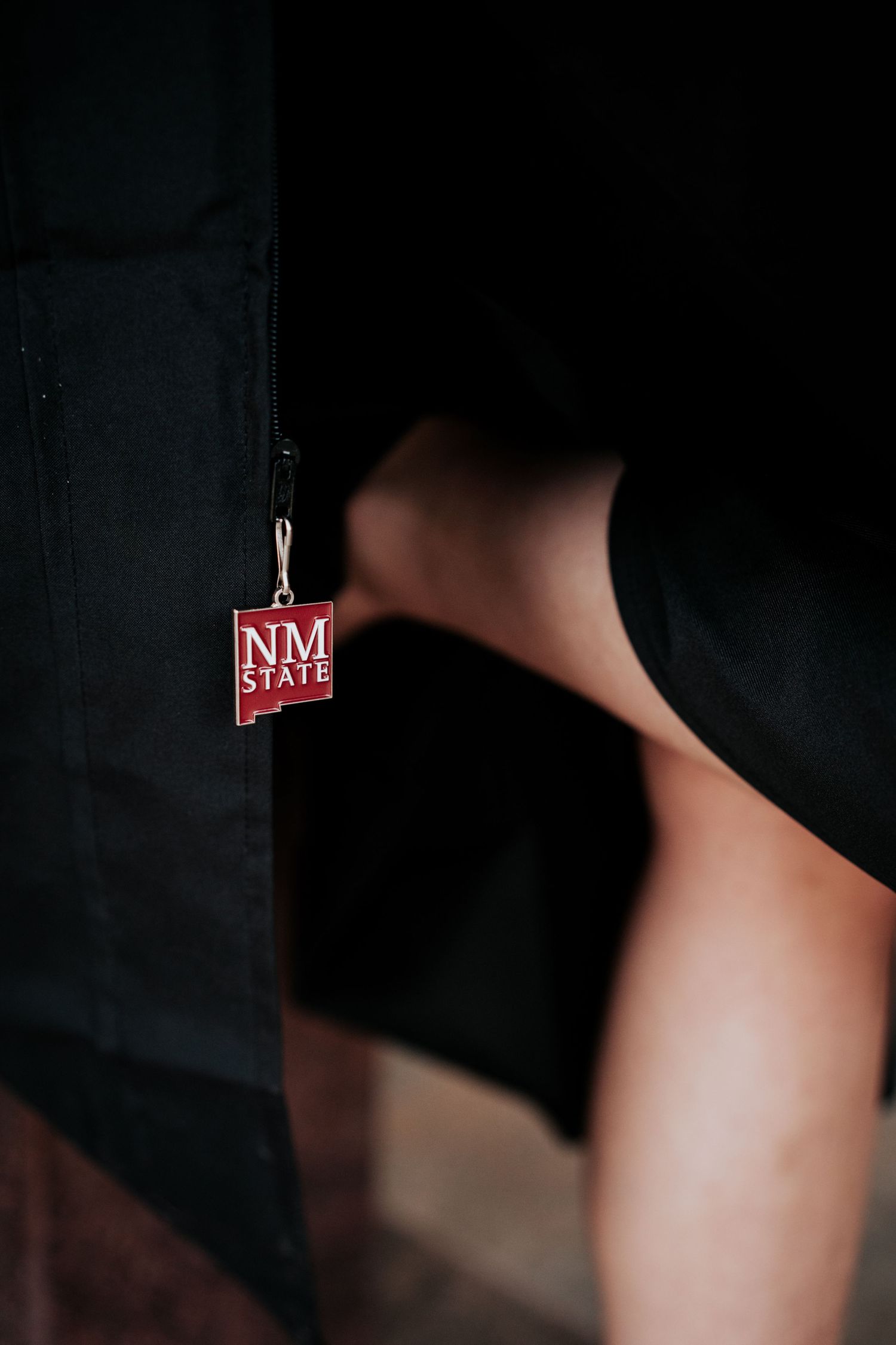 Close-up of NM State red logo charm clipped to black graduation gown.