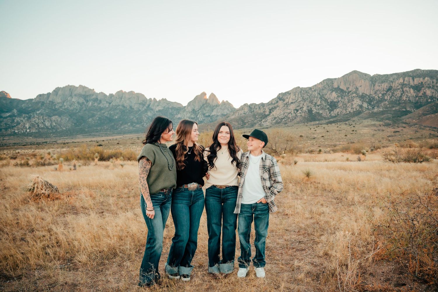 Four women laughing together in a golden desert field with the Organ Mountains in the background.