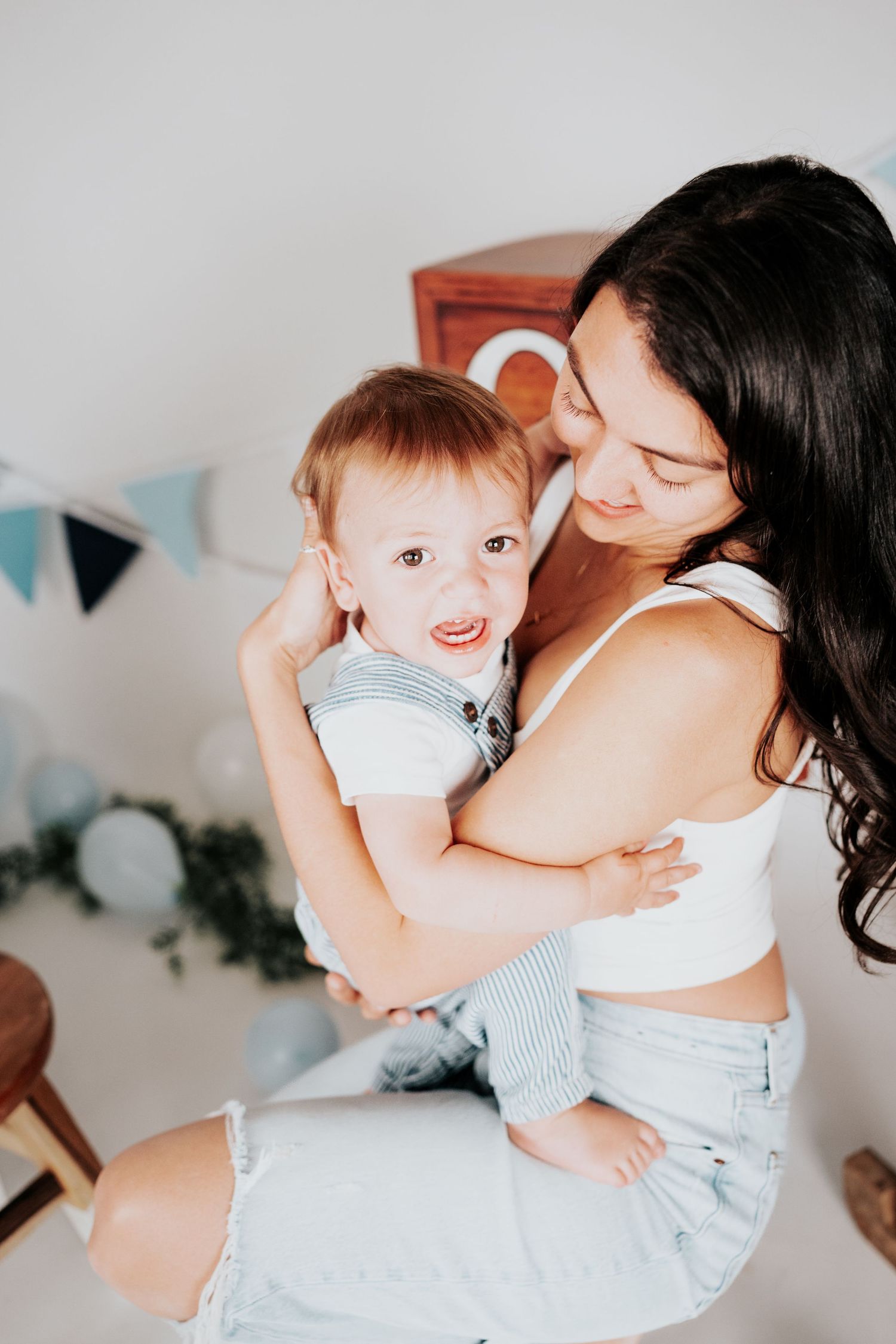 Loving mother holding her happy baby boy during a birthday photo session with blue decorations.