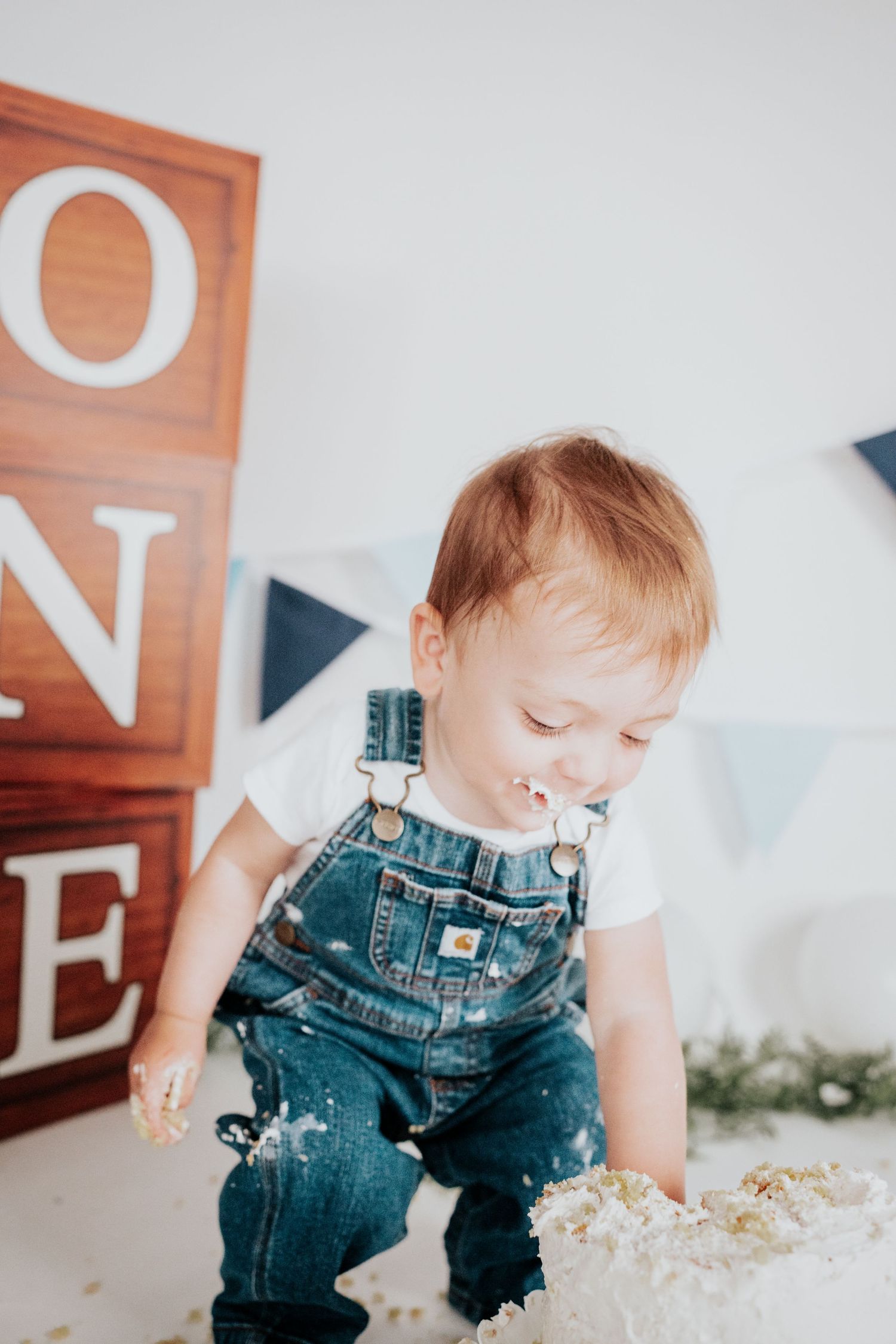 Adorable toddler in Carhartt denim overalls smiling during first birthday cake smash session.