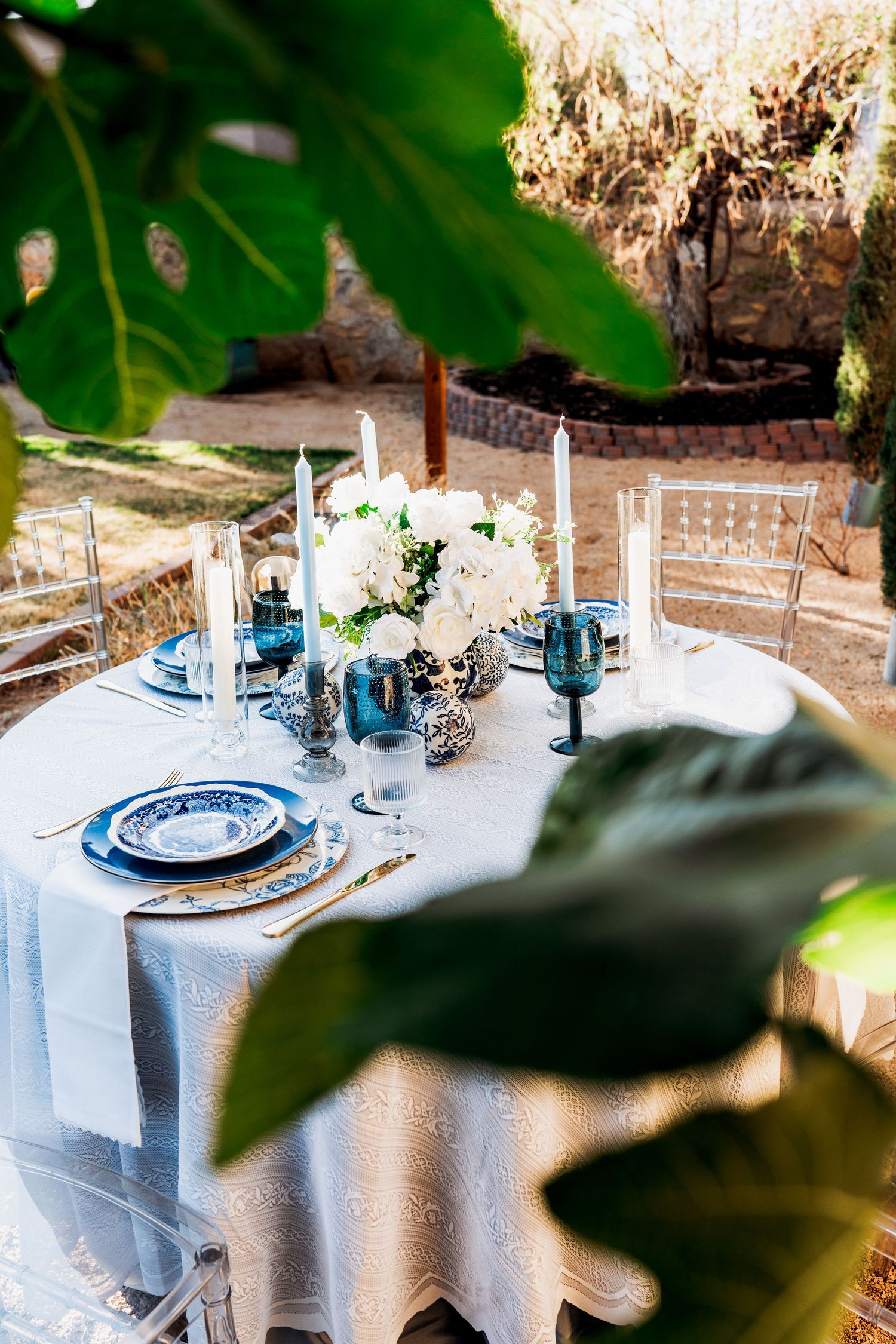 Outdoor round table with white tablecloth, blue china, candles, and white hydrangeas.
