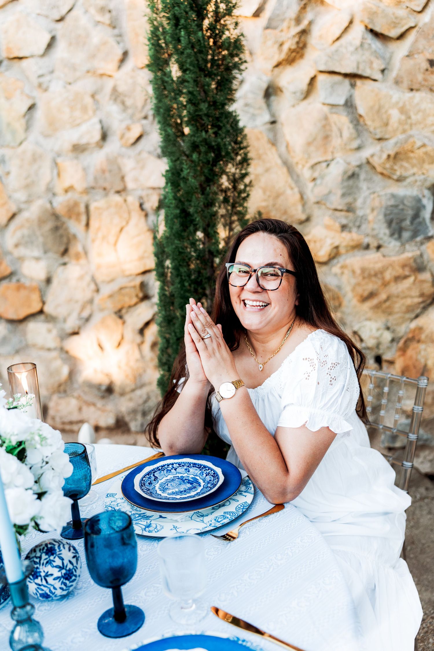 Joyful woman with glasses clapping hands at beautifully styled blue and white outdoor wedding tablescape setting.