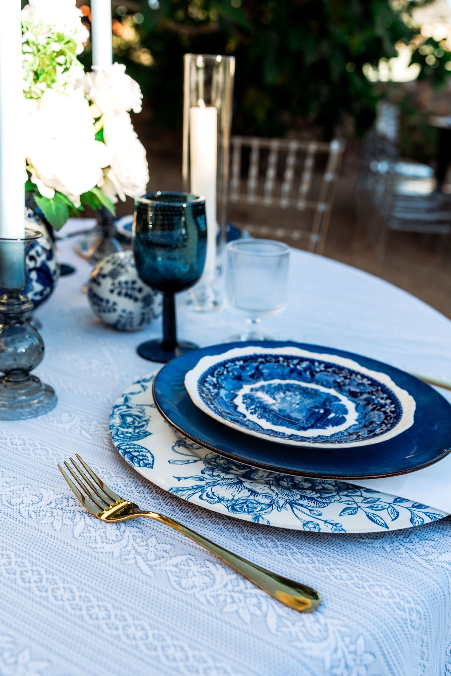 Blue and white china plate on floral charger with gold fork and blue wine glass.