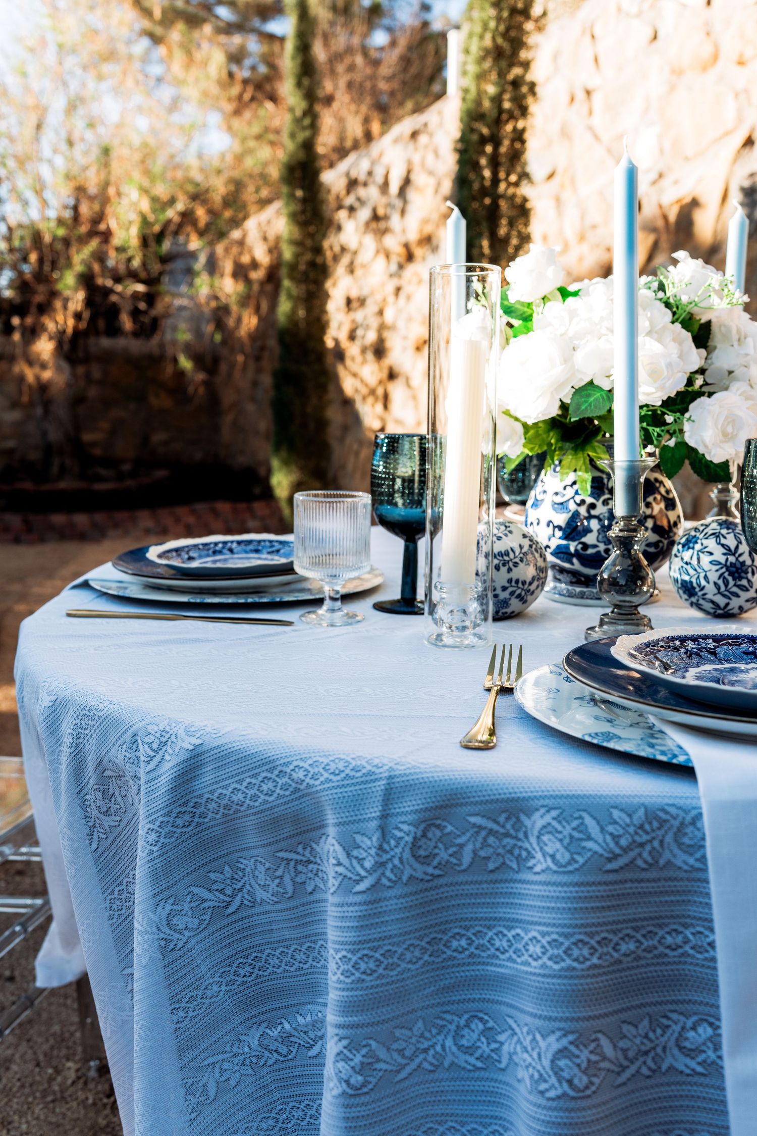 Elegant outdoor table set with blue and white china, candles, and white hydrangeas.
