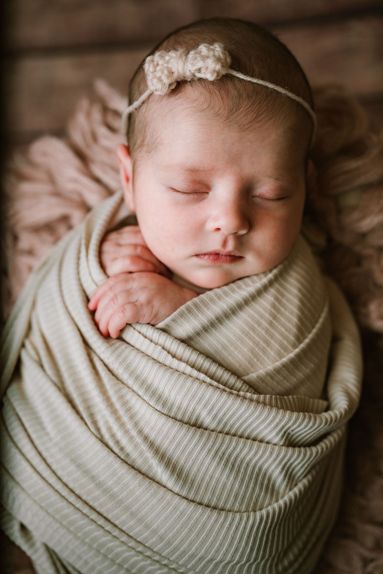 Sleeping newborn baby girl swaddled in green striped wrap with delicate floral headband.