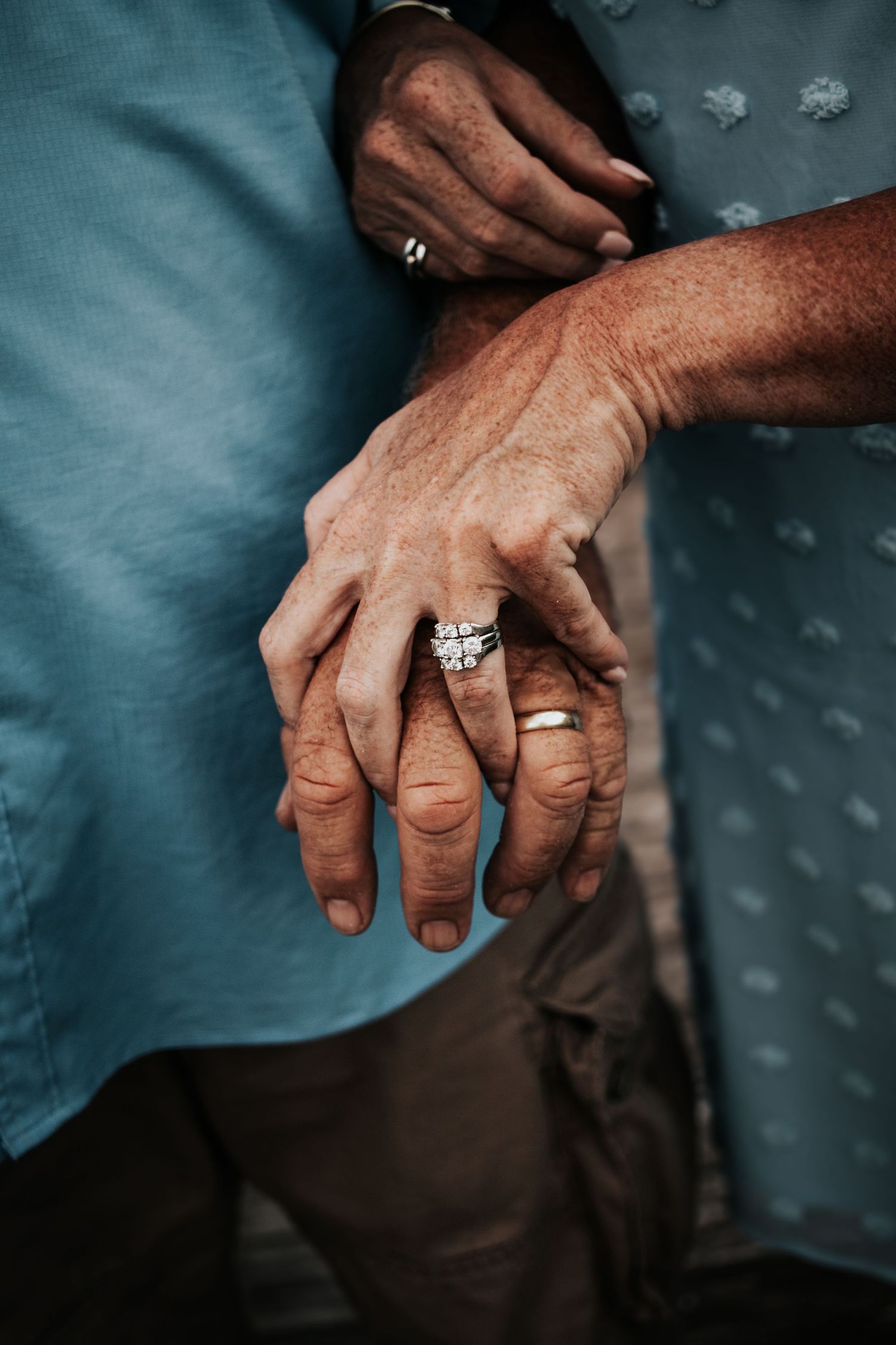 Close-up of married couple's intertwined hands showing diamond engagement and wedding bands.