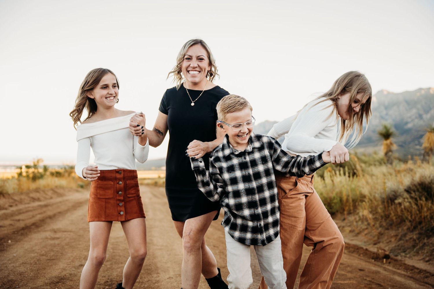 Laughing mother and three kids walking together on a scenic desert dirt road.