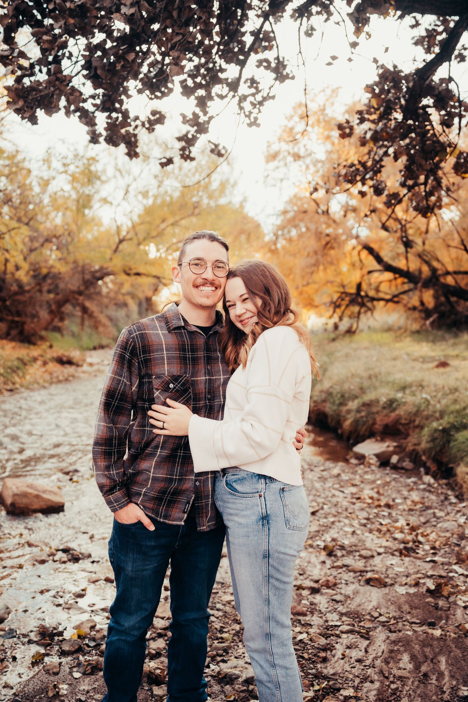 Couple embracing and smiling by a rocky creek surrounded by autumn foliage.