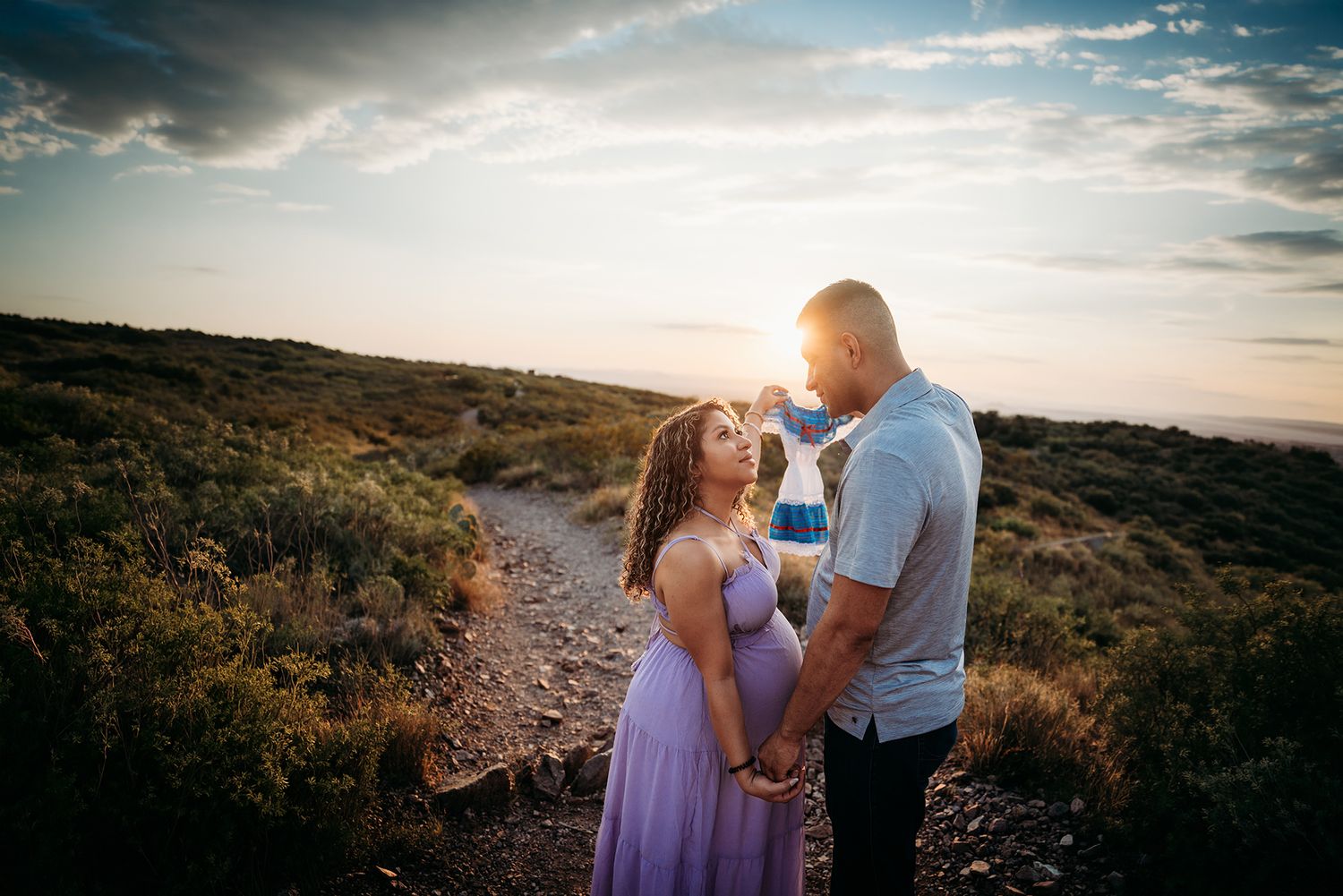 Couple sharing a romantic moment at sunset on a scenic hilltop trail, woman in lavender dress.