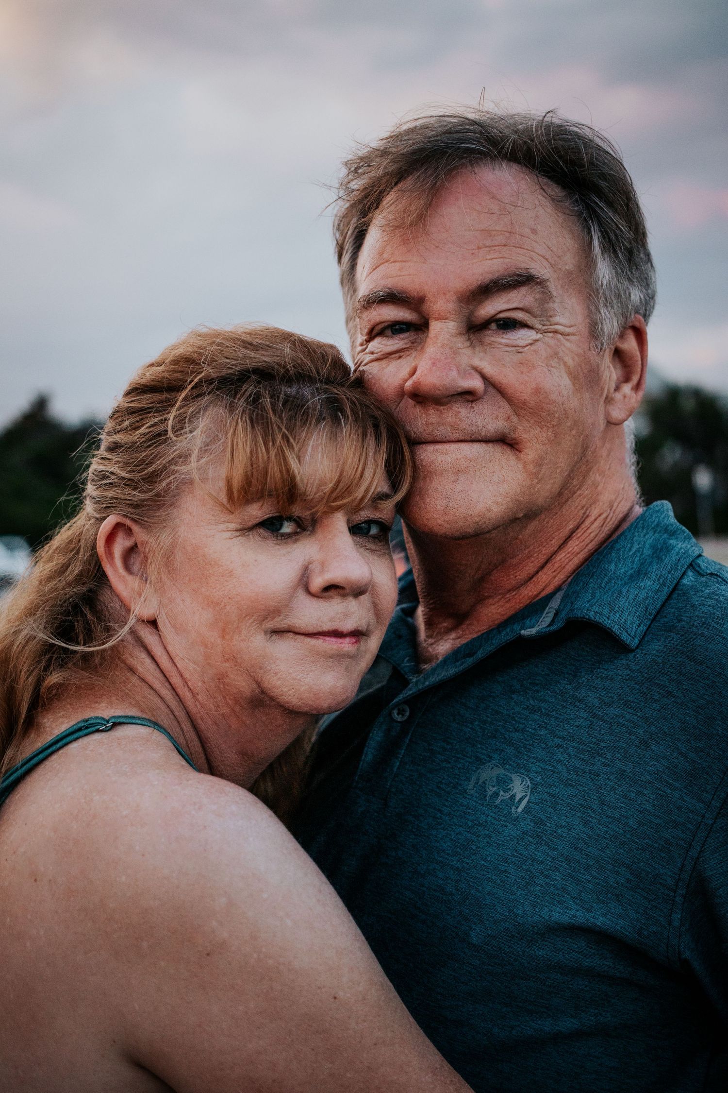 Close-up portrait of a smiling middle-aged couple cheek to cheek outdoors at sunset.