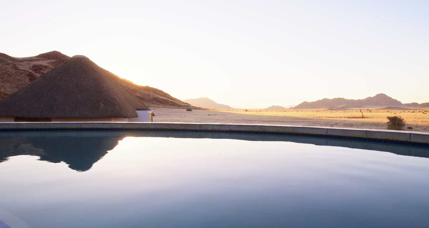 Infinity pool reflecting desert mountains at golden sunset with lone figure standing at the edge.