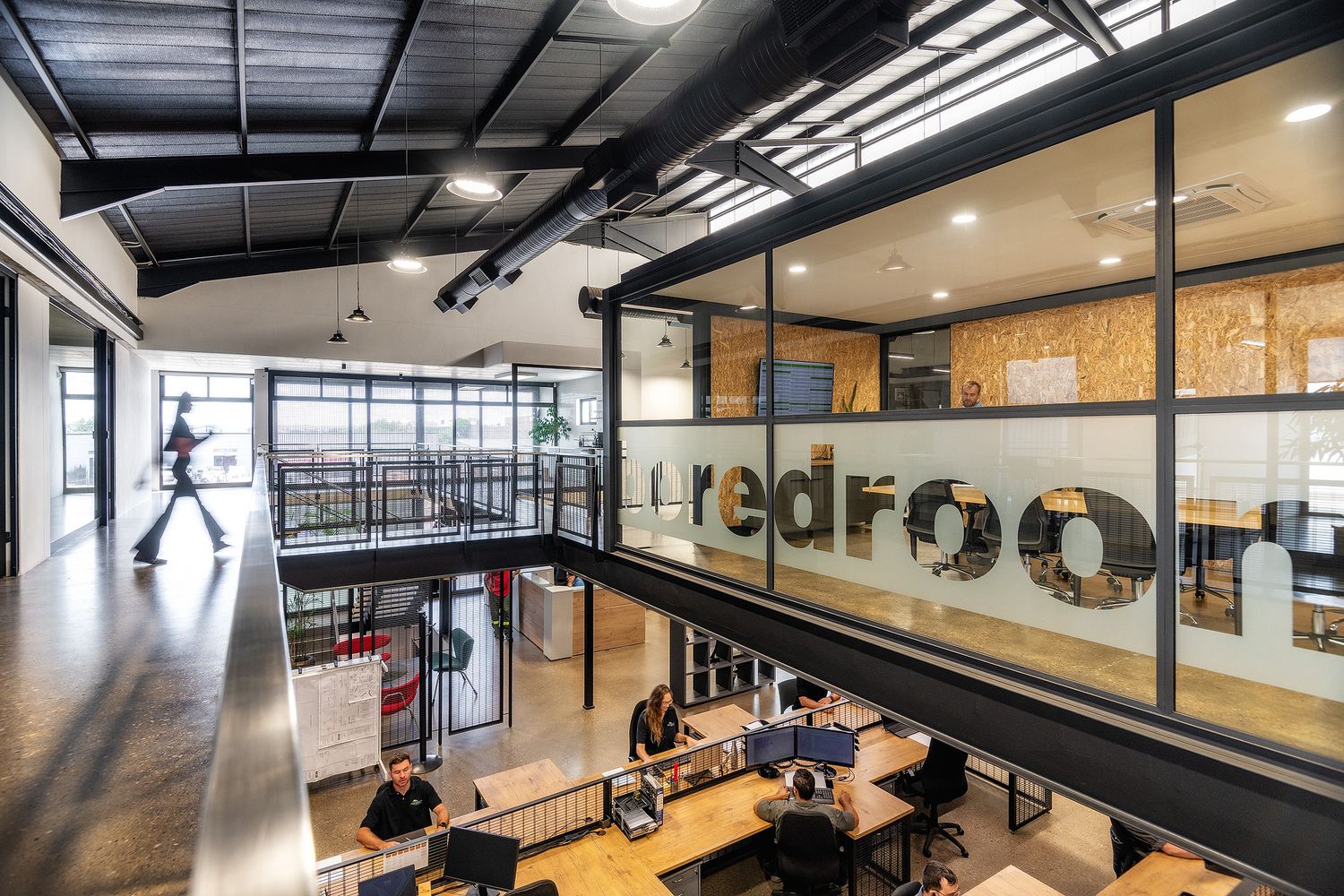 Modern two-story coworking office space with glass walls, exposed ceilings, and professionals working at open desks.
