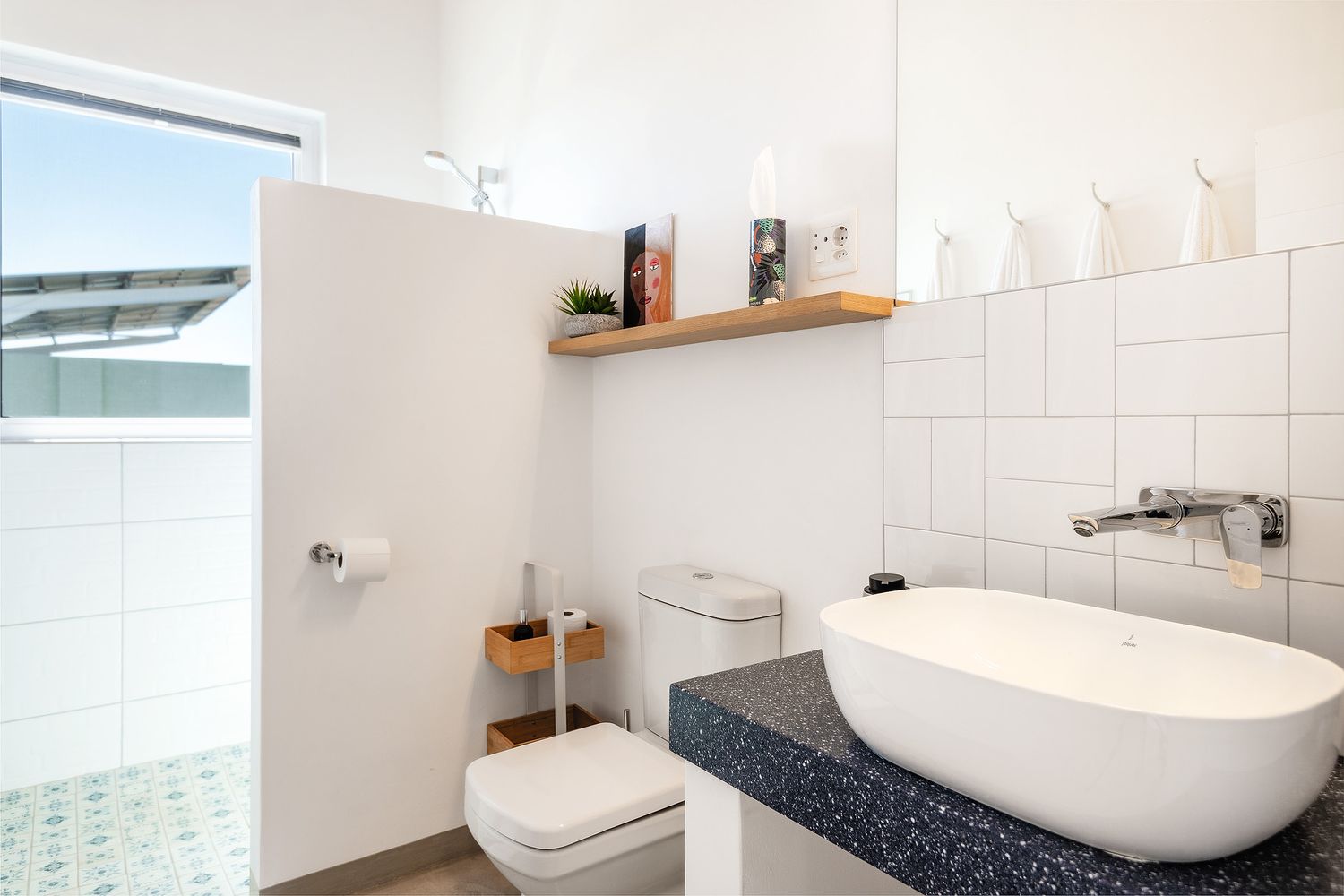 Modern white bathroom with vessel sink, granite countertop, wall-mounted faucet, toilet, and natural light from window.