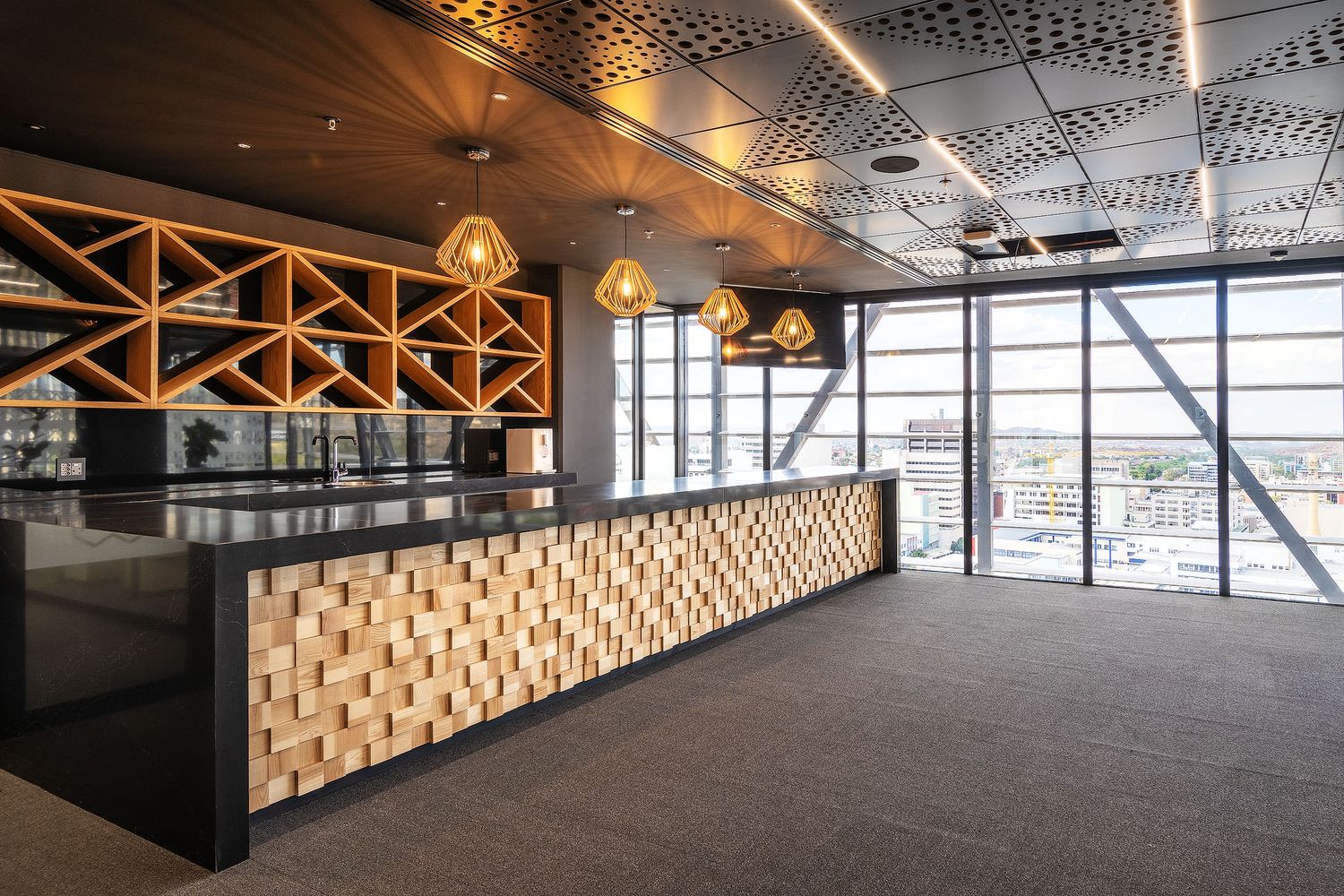 Contemporary office reception desk with geometric wood paneling and warm pendant lighting overlooking city views.
