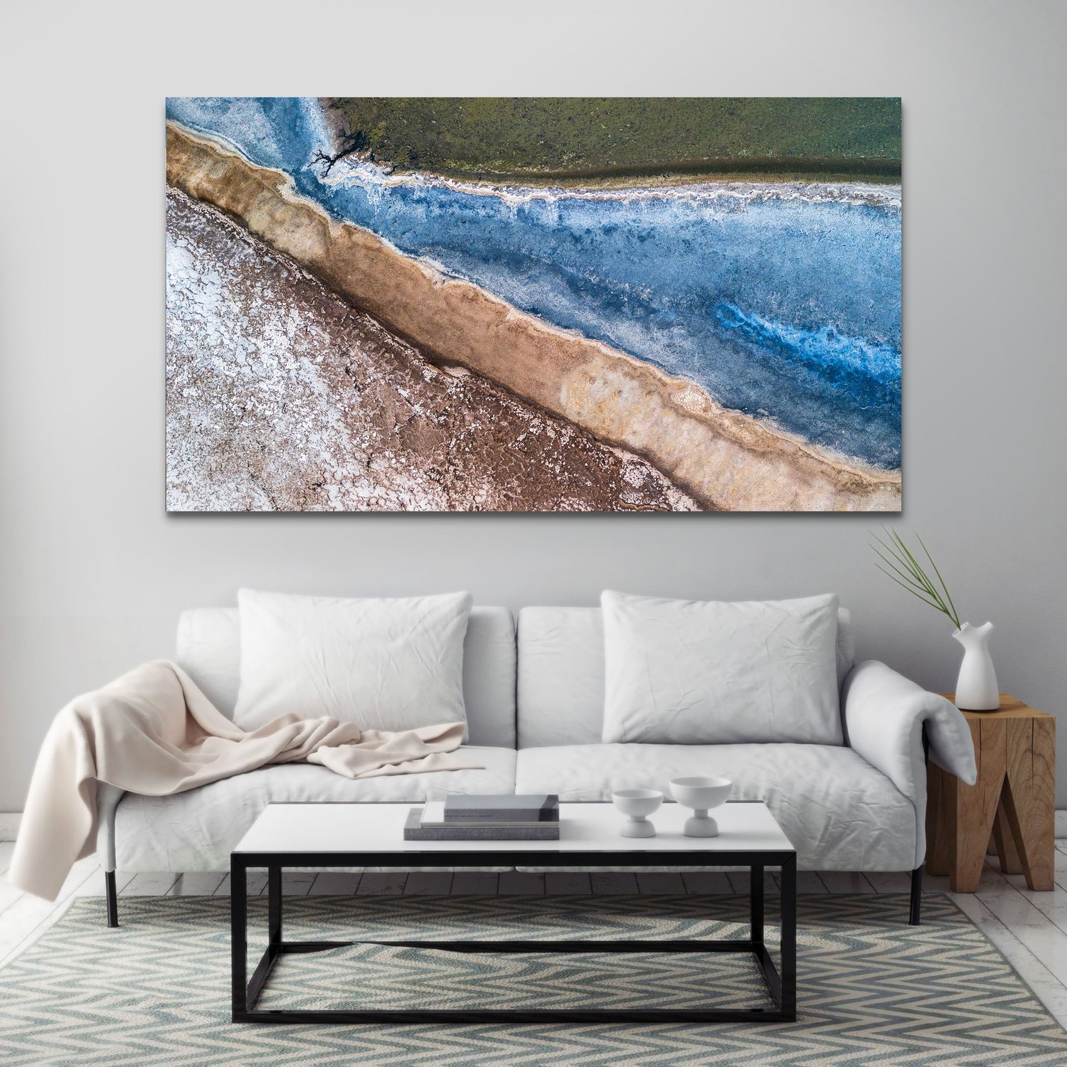 Aerial view canvas wall art of a coastal shoreline with blue ocean waves and sandy beach above a white sofa.