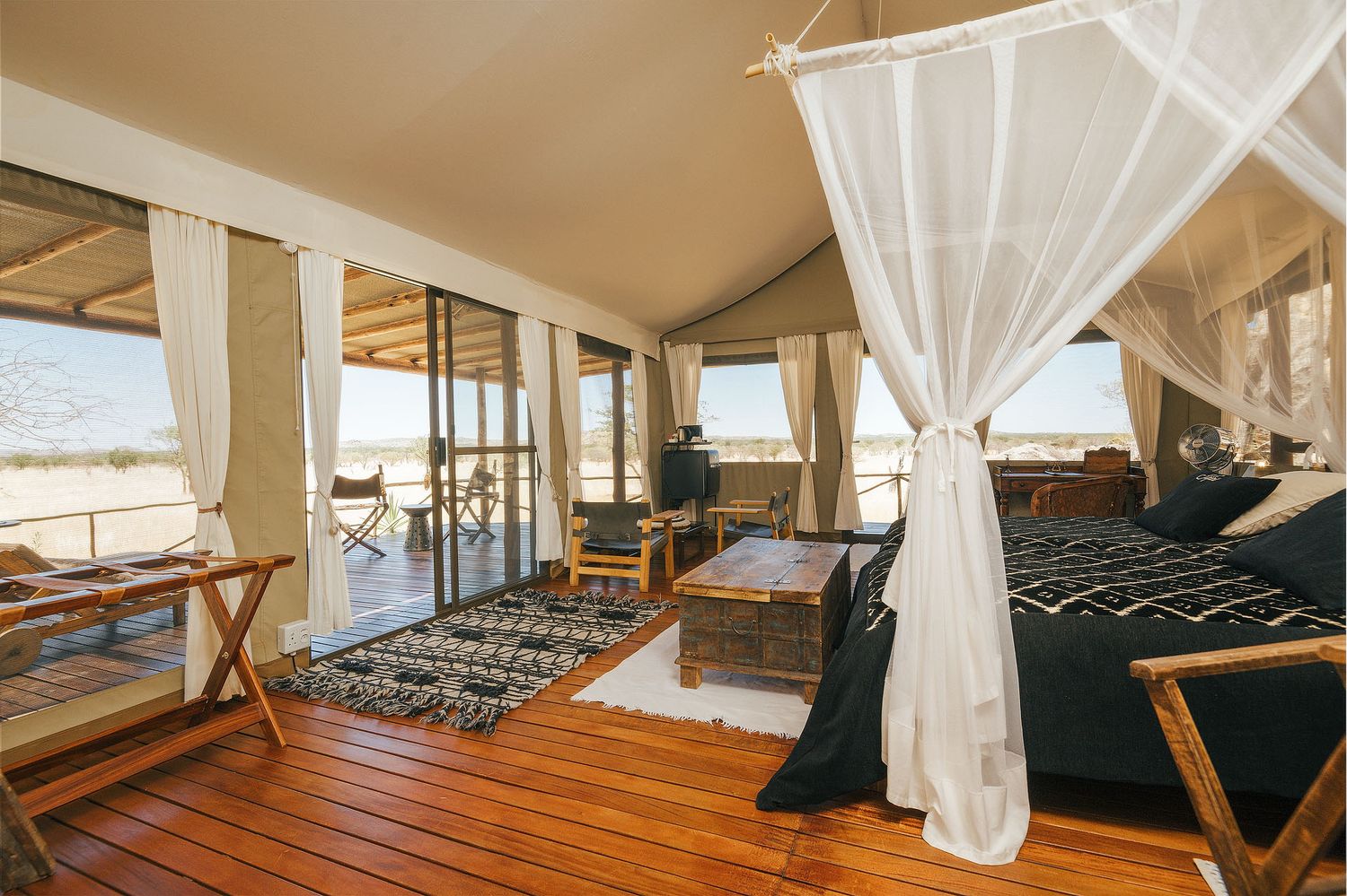 Luxury safari tent interior with canopy bed, wooden deck, and open views of the savanna landscape.